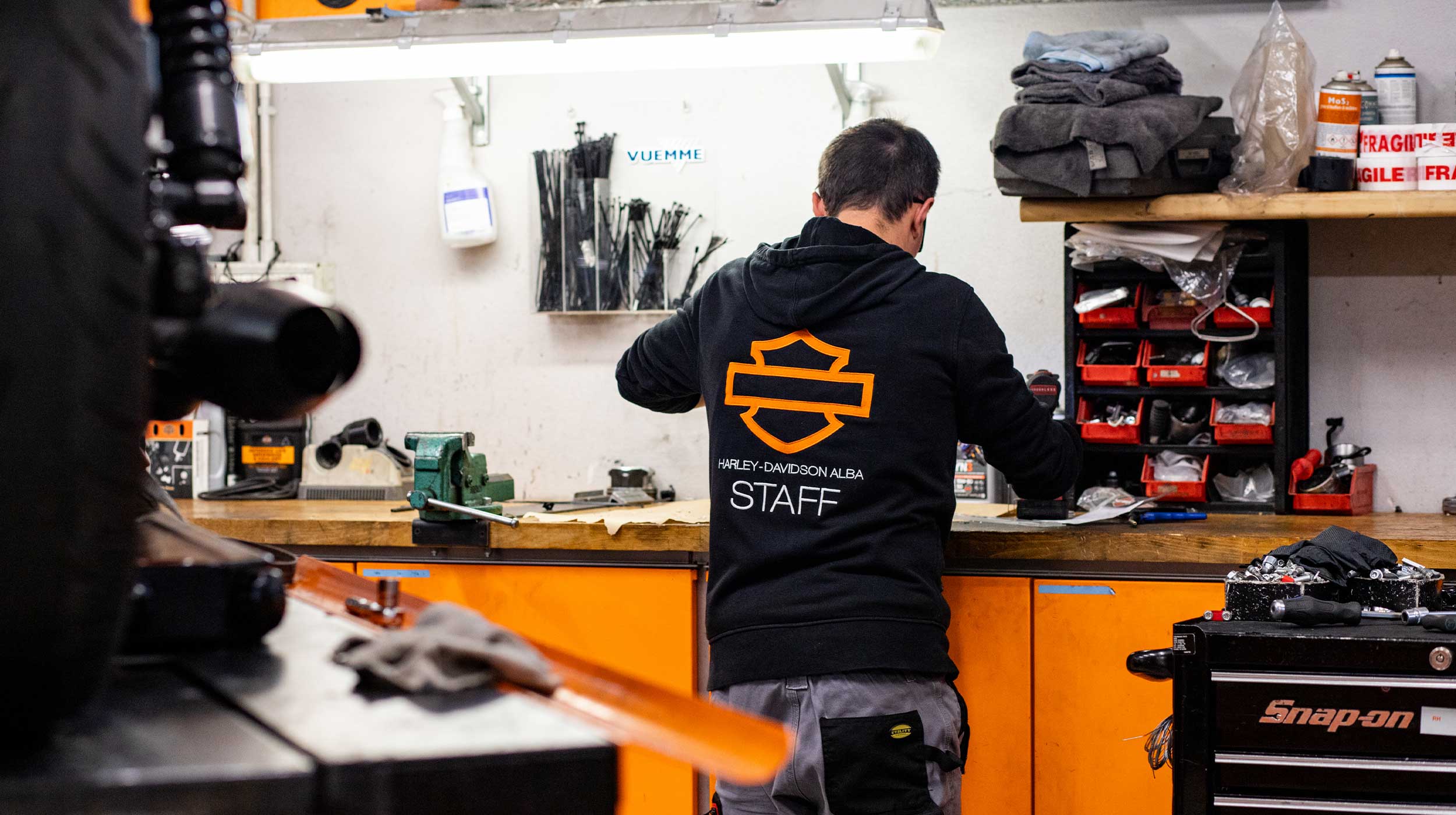 Tecnico Harley-Davidson Alba in officina, concentrato sulla manutenzione di componenti moto. Indossa abbigliamento ufficiale.