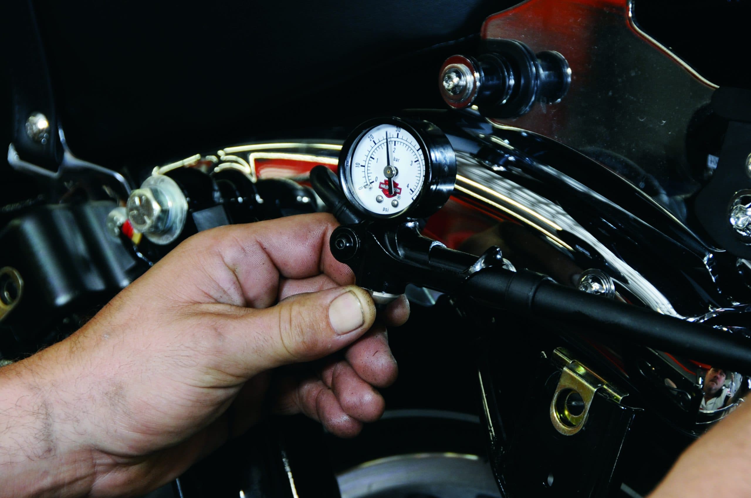 Tecnico che misura la pressione di un componente motore Harley-Davidson con un manometro, mostrando il logo e le unità psi/bar.