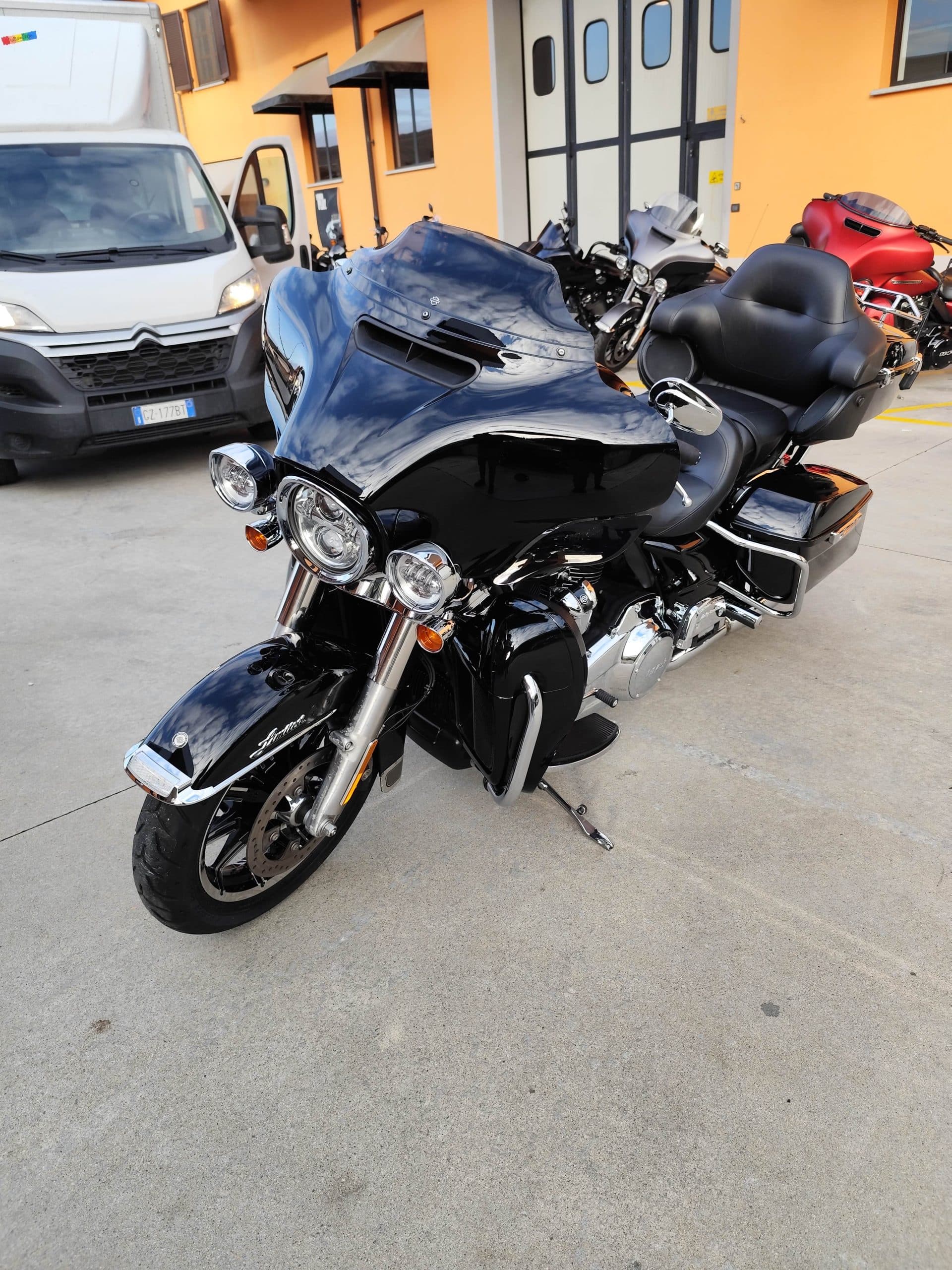 Harley-Davidson nera, modello touring, parcheggiata su cemento. Dettagli cromati e carrozzeria lucida riflettono il cielo.