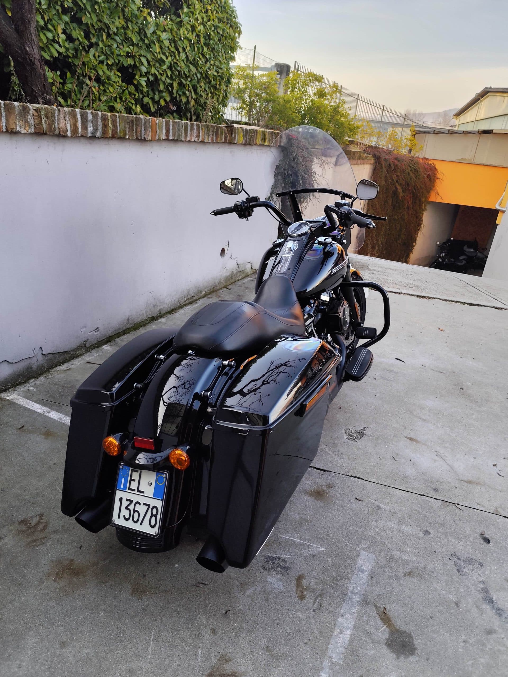 Harley-Davidson nera lucida con borse laterali rigide e parabrezza, parcheggiata. Dettagli cromati e scarichi neri. Pronta per un test ride.