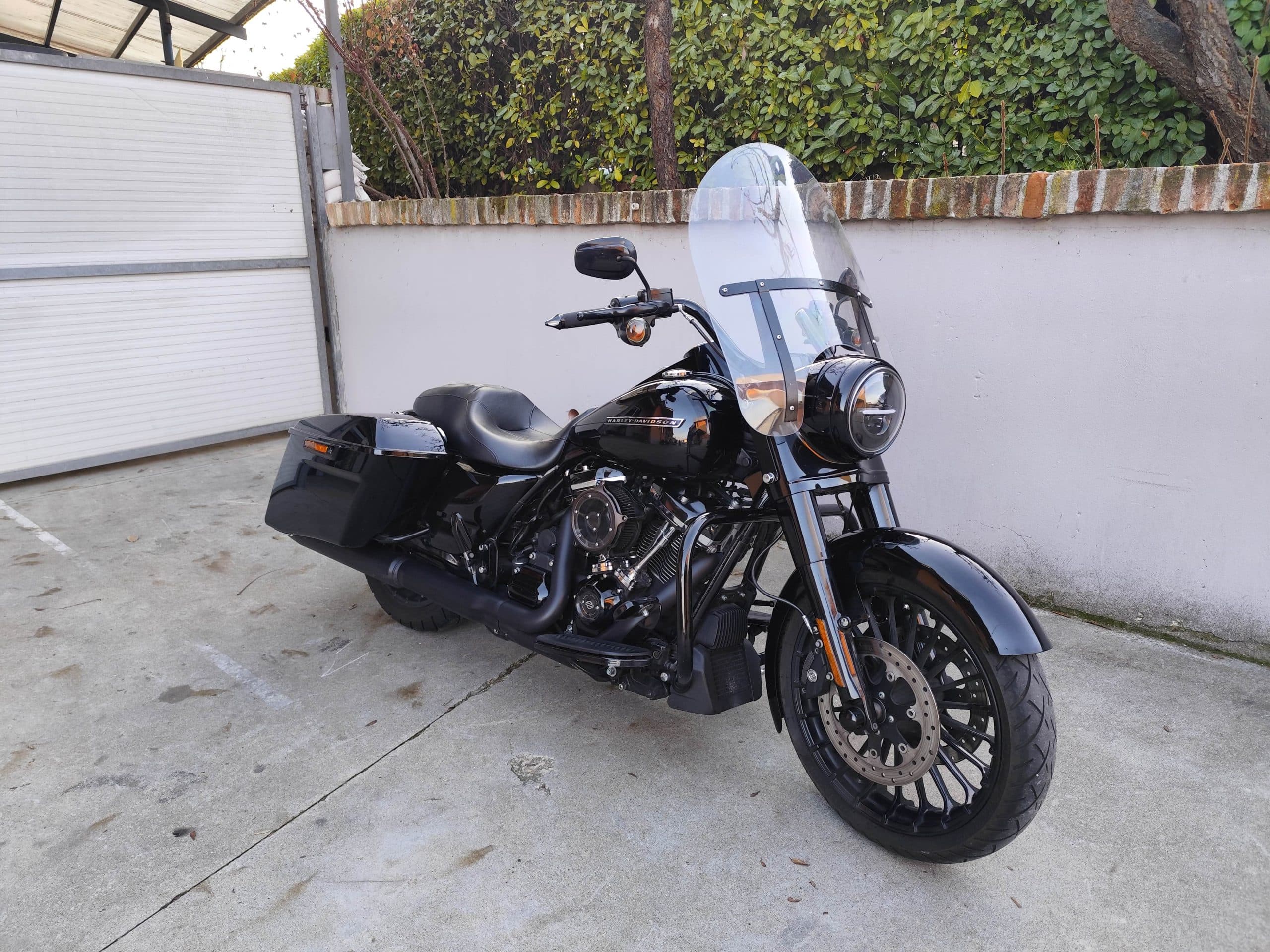 Harley-Davidson nera, modello touring con parabrezza e borse laterali, parcheggiata su cemento. Dettagli motore e scarico neri.