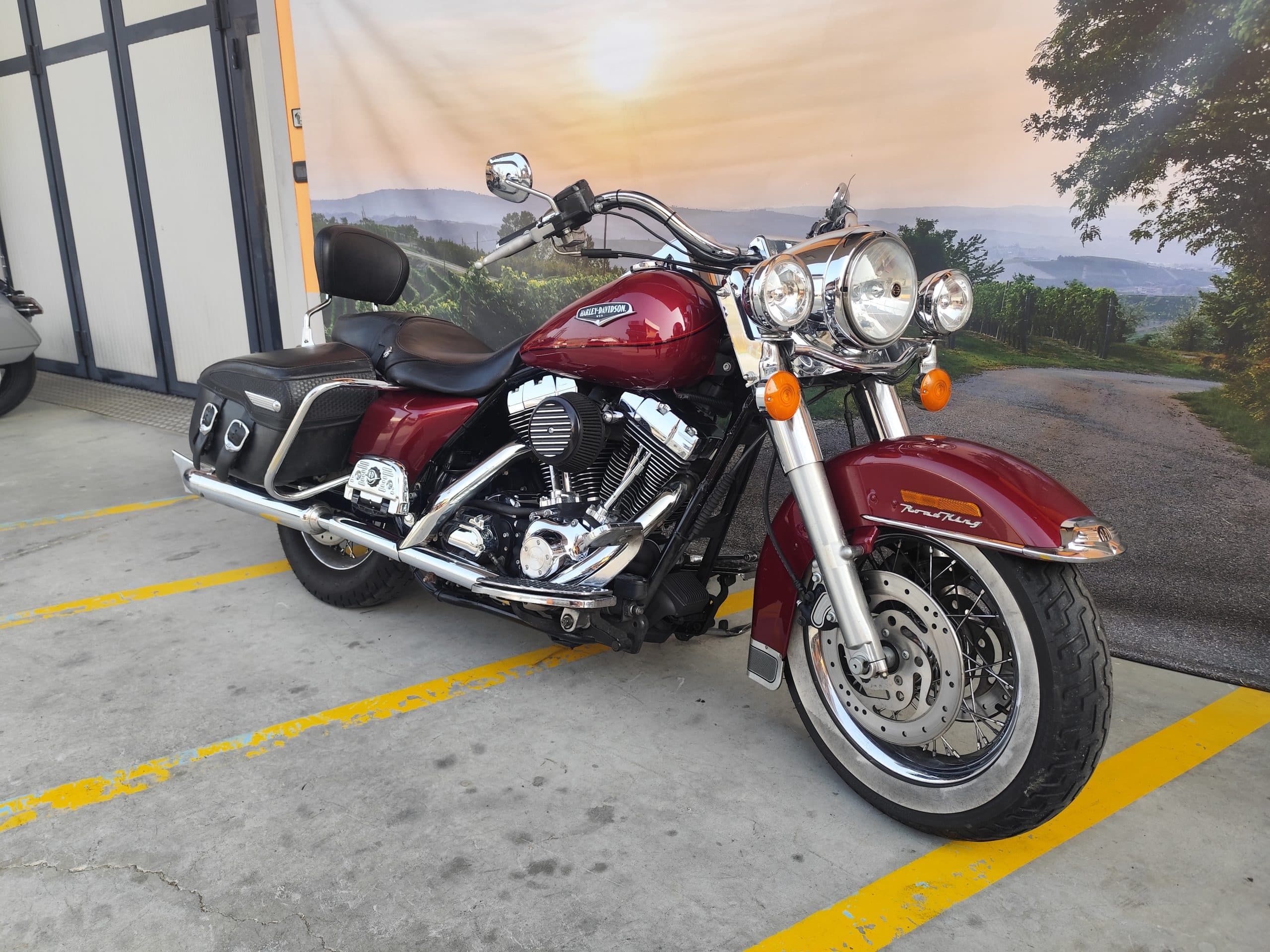 Harley-Davidson Road King rossa in esposizione, con dettagli cromati e motore V-twin, su sfondo paesaggistico. Ideale per test ride.