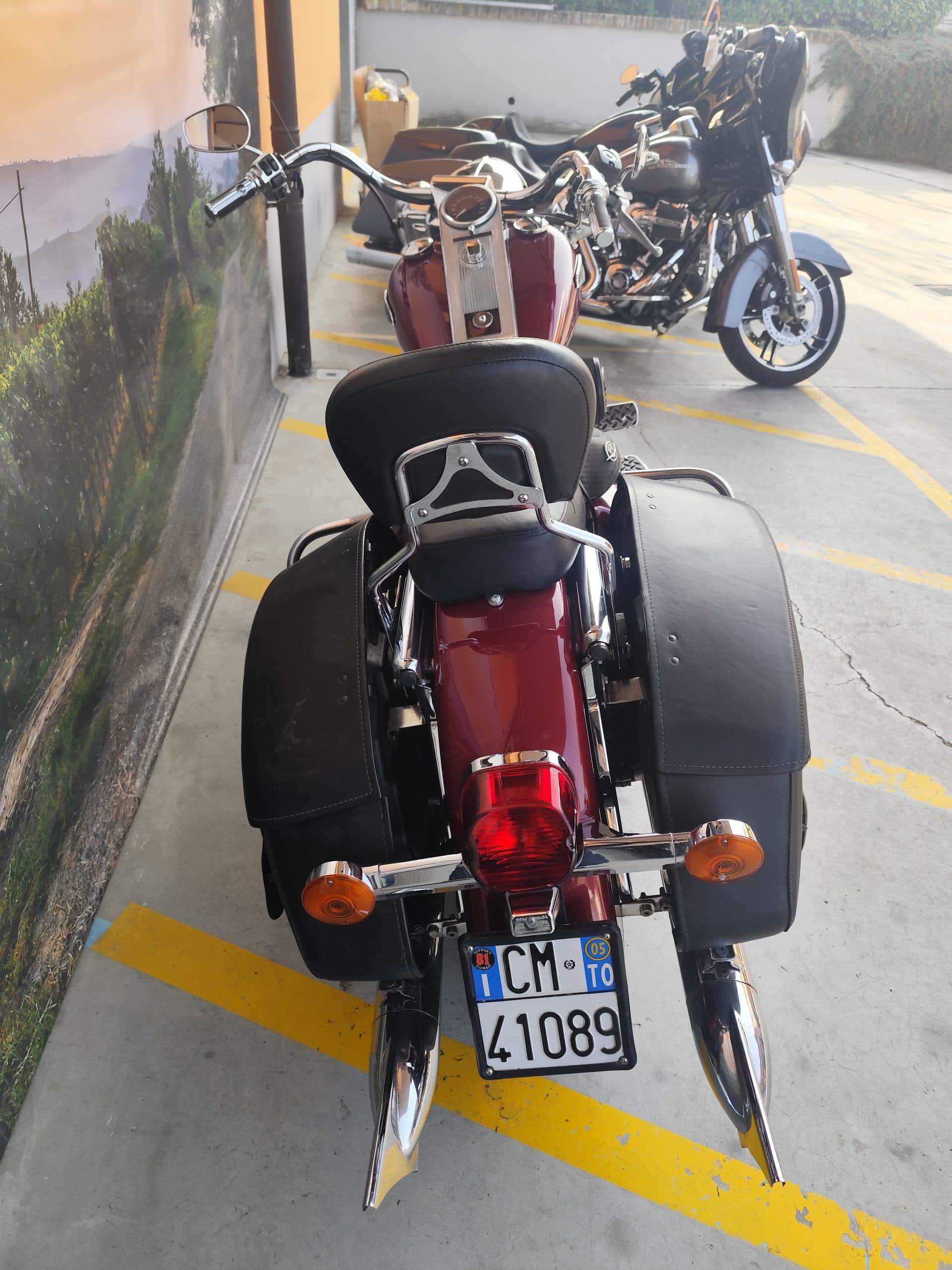 Vista posteriore di una moto Harley-Davidson rossa parcheggiata, con sella nera, borse laterali in pelle e dettagli cromati. Targa italiana visibile.