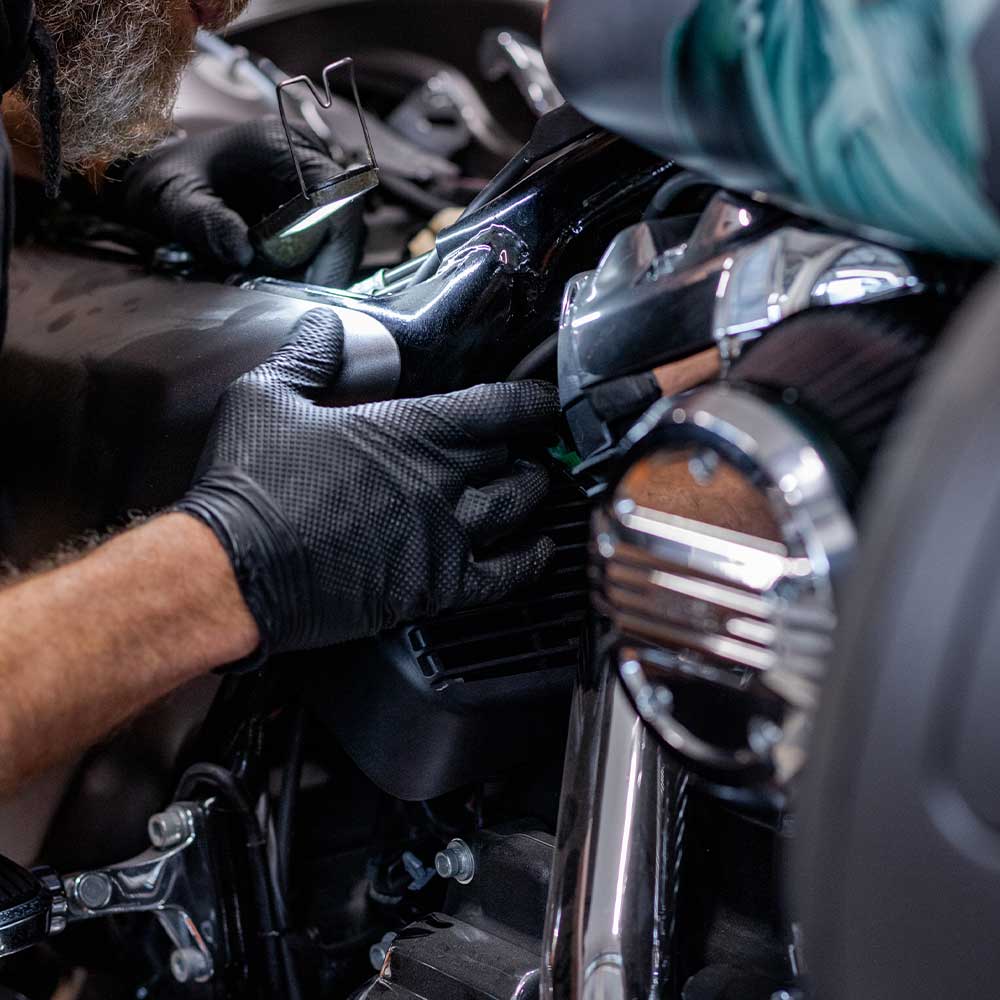 Tecnico specializzato con guanti neri esegue un'accurata ispezione e manutenzione sul motore di una moto Harley-Davidson.
