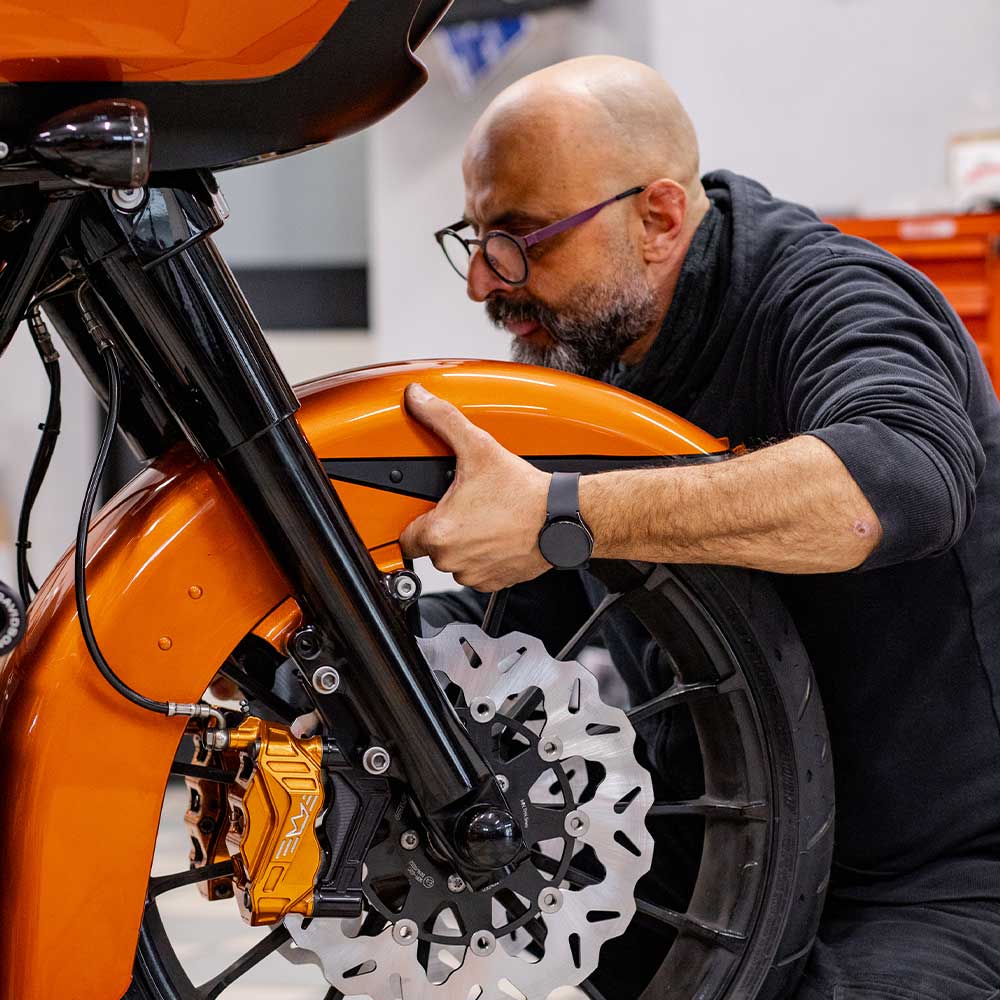 Tecnico specializzato che lavora sul parafango anteriore e sul sistema frenante di una moto Harley-Davidson custom arancione.