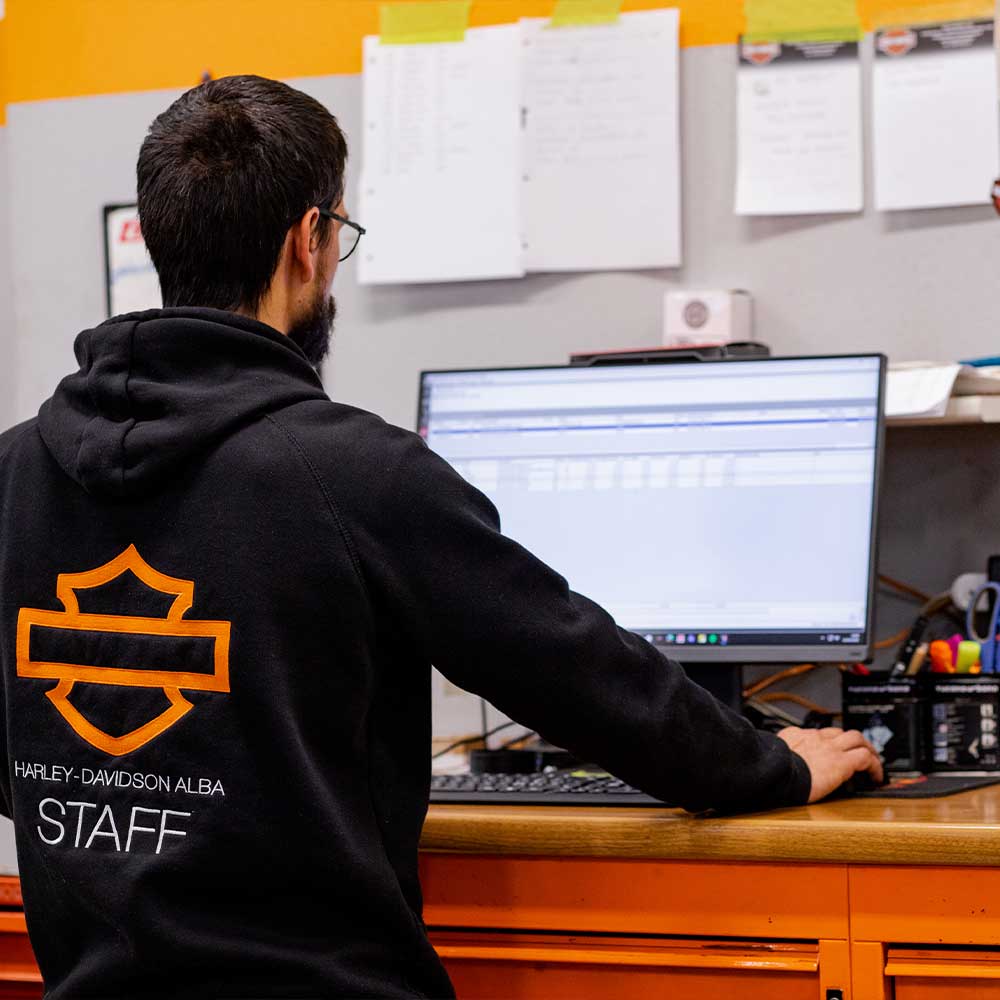 Membro dello staff Harley-Davidson Alba con abbigliamento ufficiale, che gestisce le operazioni del concessionario al computer.