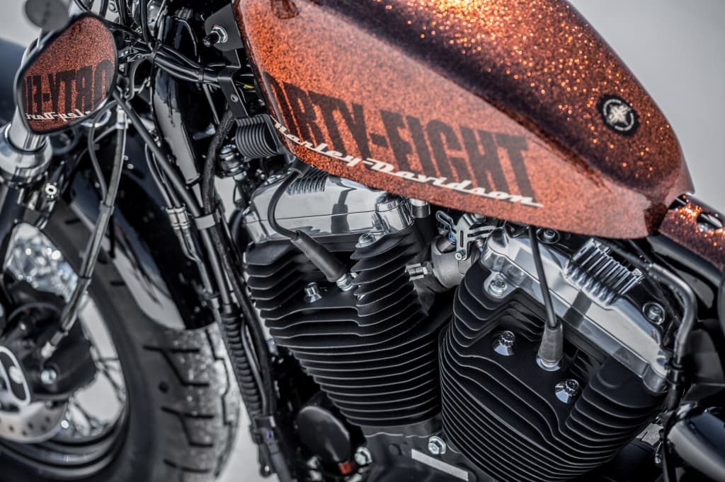 Dettaglio ravvicinato di una moto Harley-Davidson Forty-Eight, con serbatoio glitterato color rame e motore V-twin con finiture cromate.