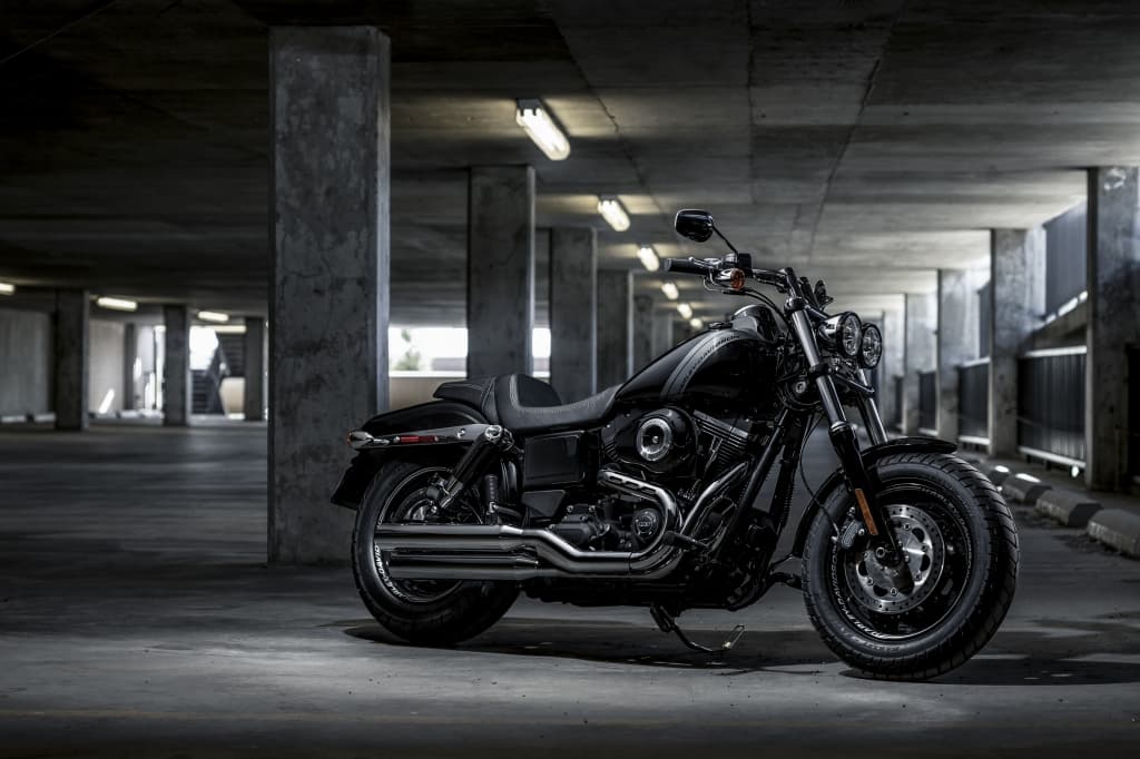 Harley-Davidson nera, modello cruiser, parcheggiata in un garage sotterraneo in cemento. Dettagli cromati e pneumatici robusti.