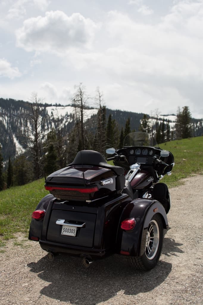 Harley-Davidson Tri Glide Ultra bordeaux, vista posteriore, su strada sterrata. Sfondo montano innevato. Perfetta per test ride e viaggi.