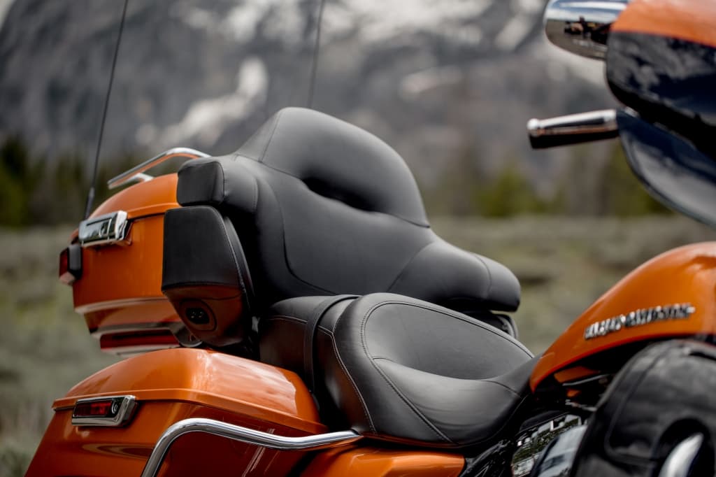 Dettaglio sella biposto in pelle nera, top case e borse laterali arancioni di una moto touring Harley-Davidson, con cromature e logo sul serbatoio, ideale per test ride.
