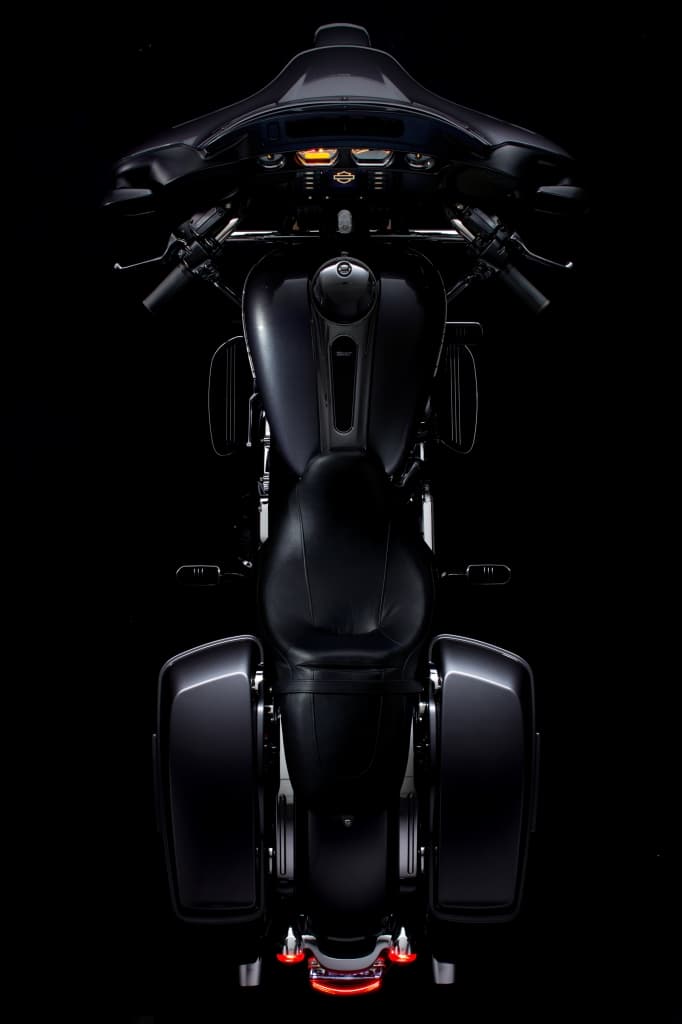 Harley-Davidson touring scura, vista zenitale. Dettagli di carena, cruscotto con indicatori accesi, serbatoio, sella e borse laterali. Fanale posteriore illuminato.