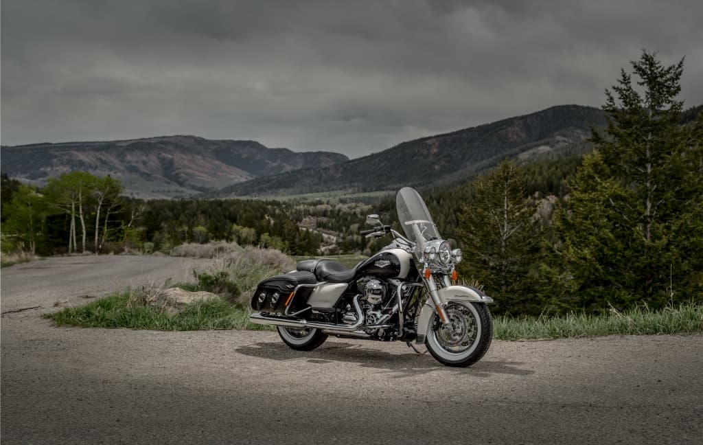 Harley-Davidson touring bicolore con parabrezza e borse laterali, parcheggiata su strada montana. Pronta per un test ride.