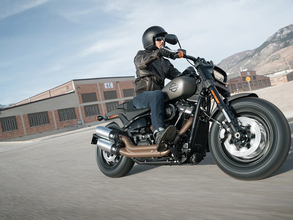 Motociclista con casco e abbigliamento tecnico su Harley-Davidson in movimento. La moto, con motore V-twin, è su strada asfaltata.
