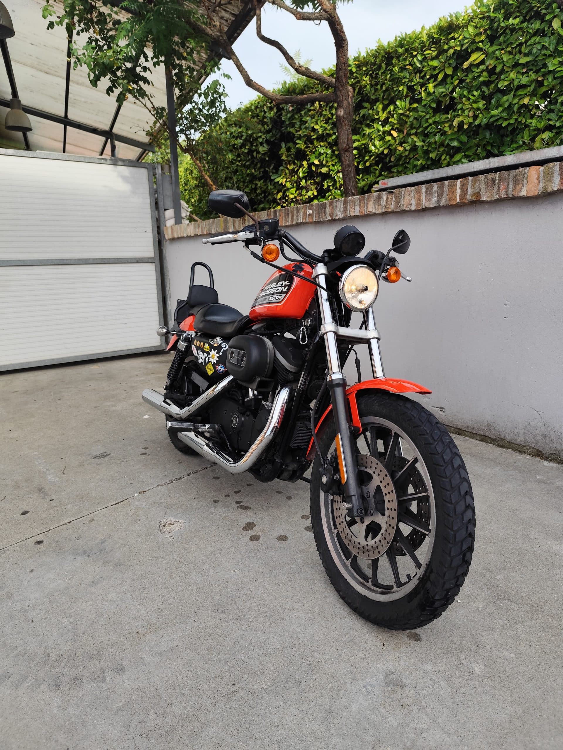 Harley-Davidson 883R arancione con scarichi cromati, motore nero e pneumatici tassellati, parcheggiata su pavimentazione in cemento.