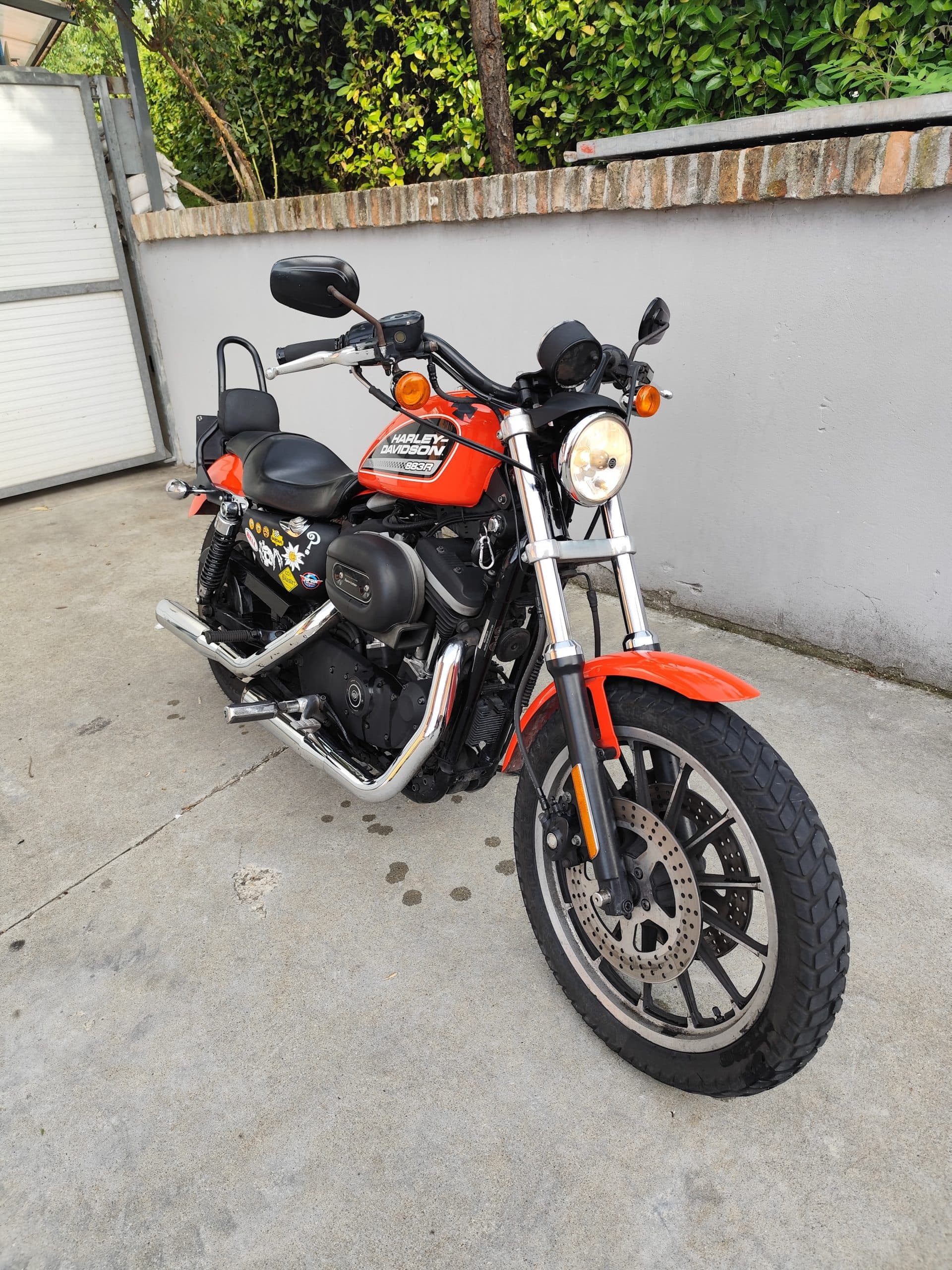 Harley-Davidson Sportster 883R arancione, con serbatoio e parafango in tinta, motore nero, scarichi cromati e adesivi. Faro acceso.