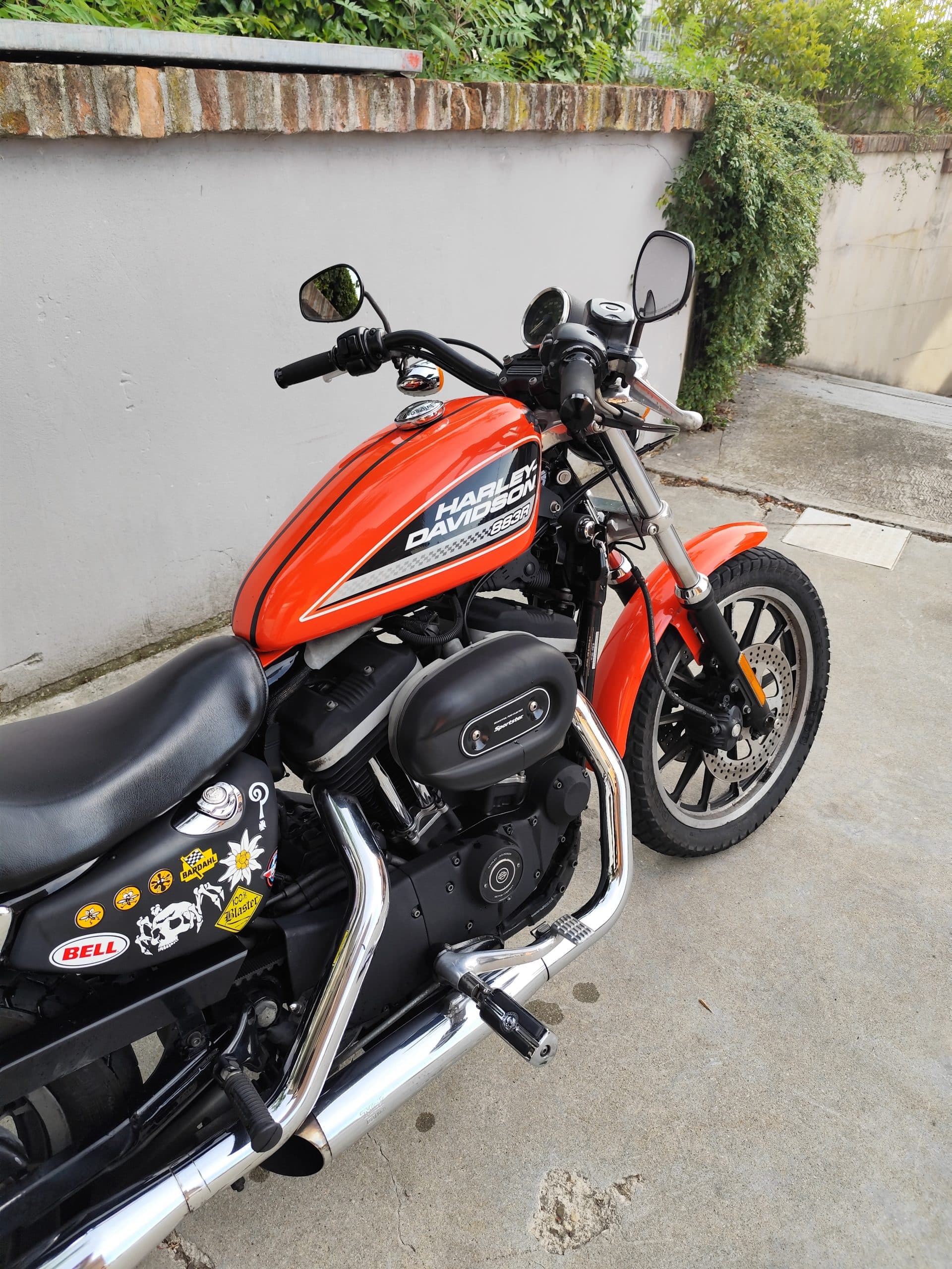 Harley-Davidson Sportster 883R con serbatoio arancione, motore V-Twin nero, scarichi cromati e dettagli personalizzati.