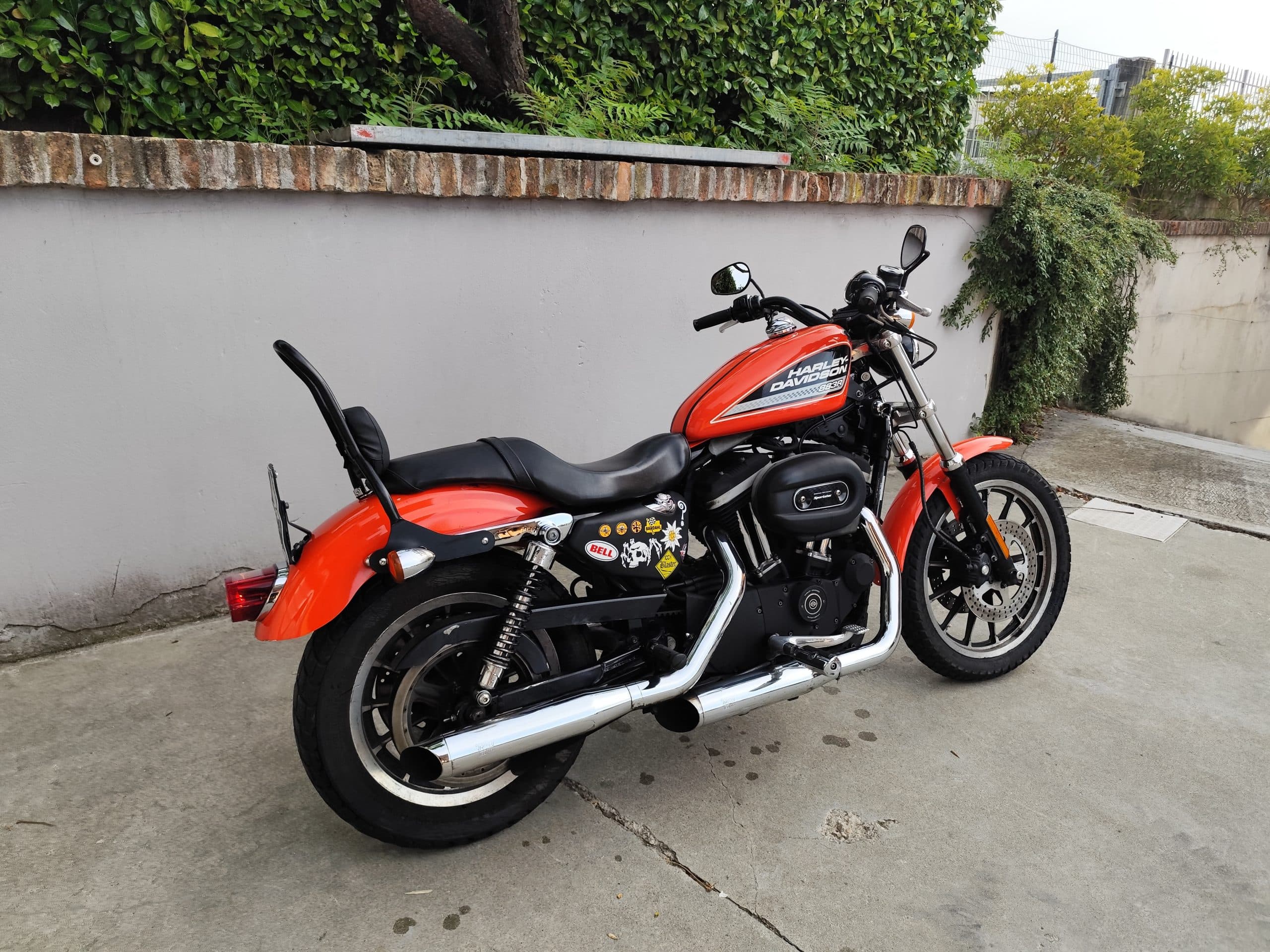 Harley-Davidson Sportster 883R arancione, con motore nero, scarichi cromati e adesivi personalizzati. Perfetta per test ride.