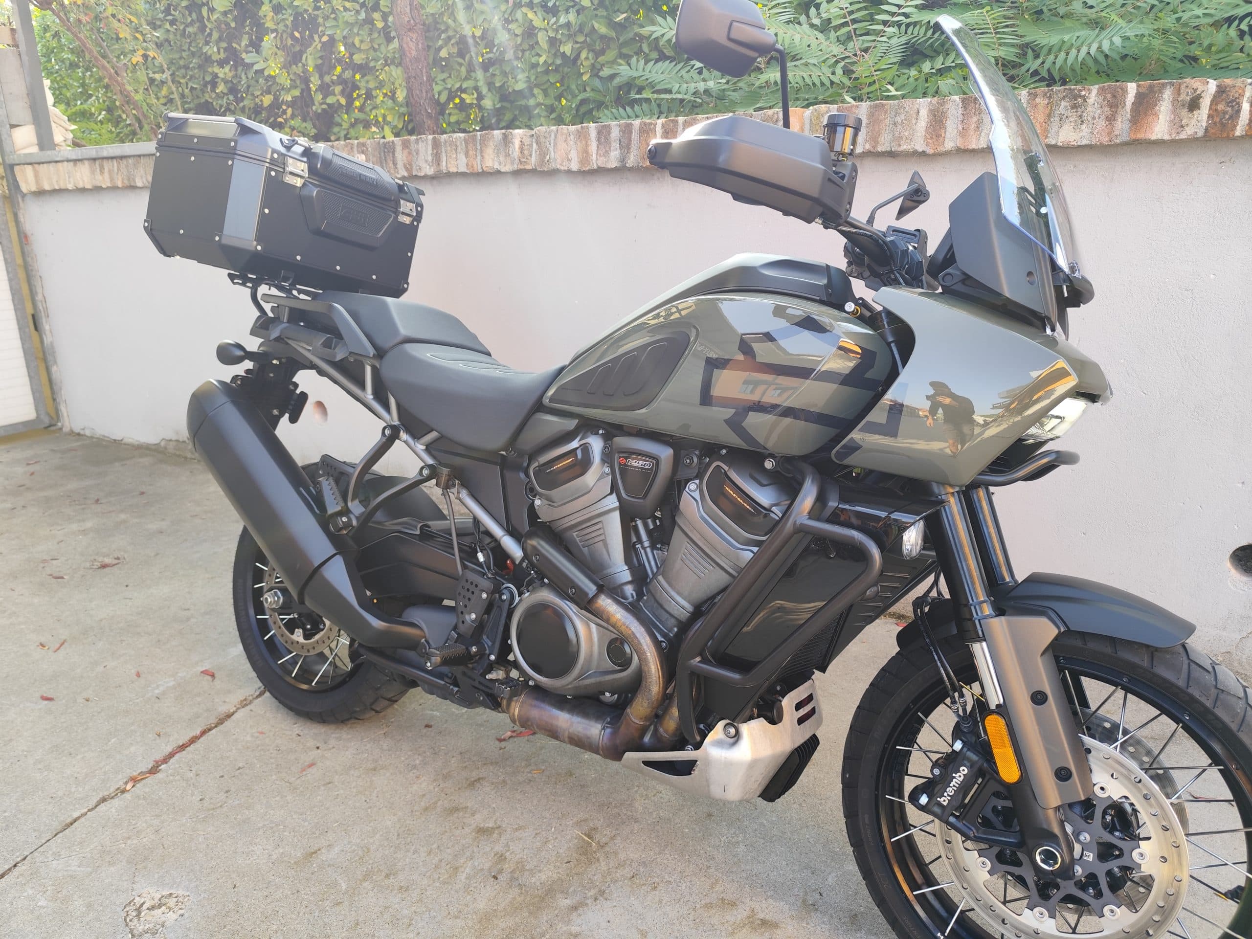 Harley-Davidson Pan America 1250 Special verde militare con top case, paramani e barre paramotore, parcheggiata all'aperto. Ideale per test ride.