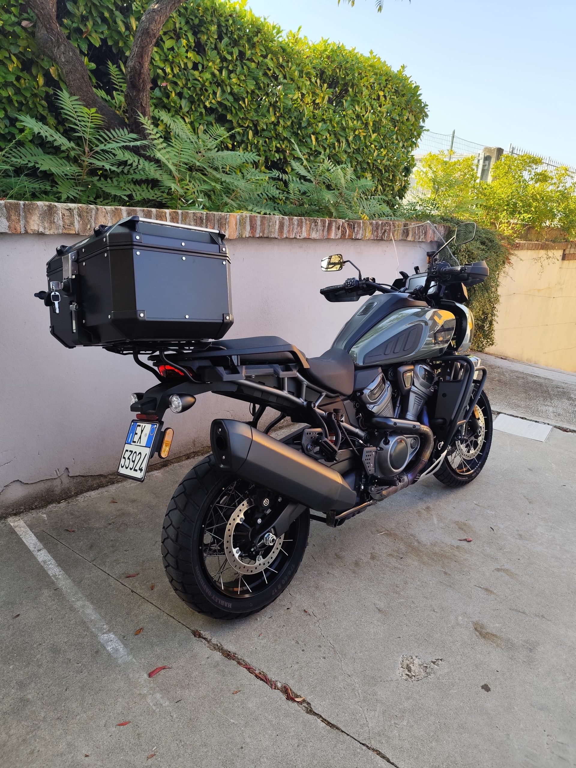 Moto Harley-Davidson Pan America, modello adventure touring, equipaggiata con top case nero, parcheggiata su pavimentazione esterna.