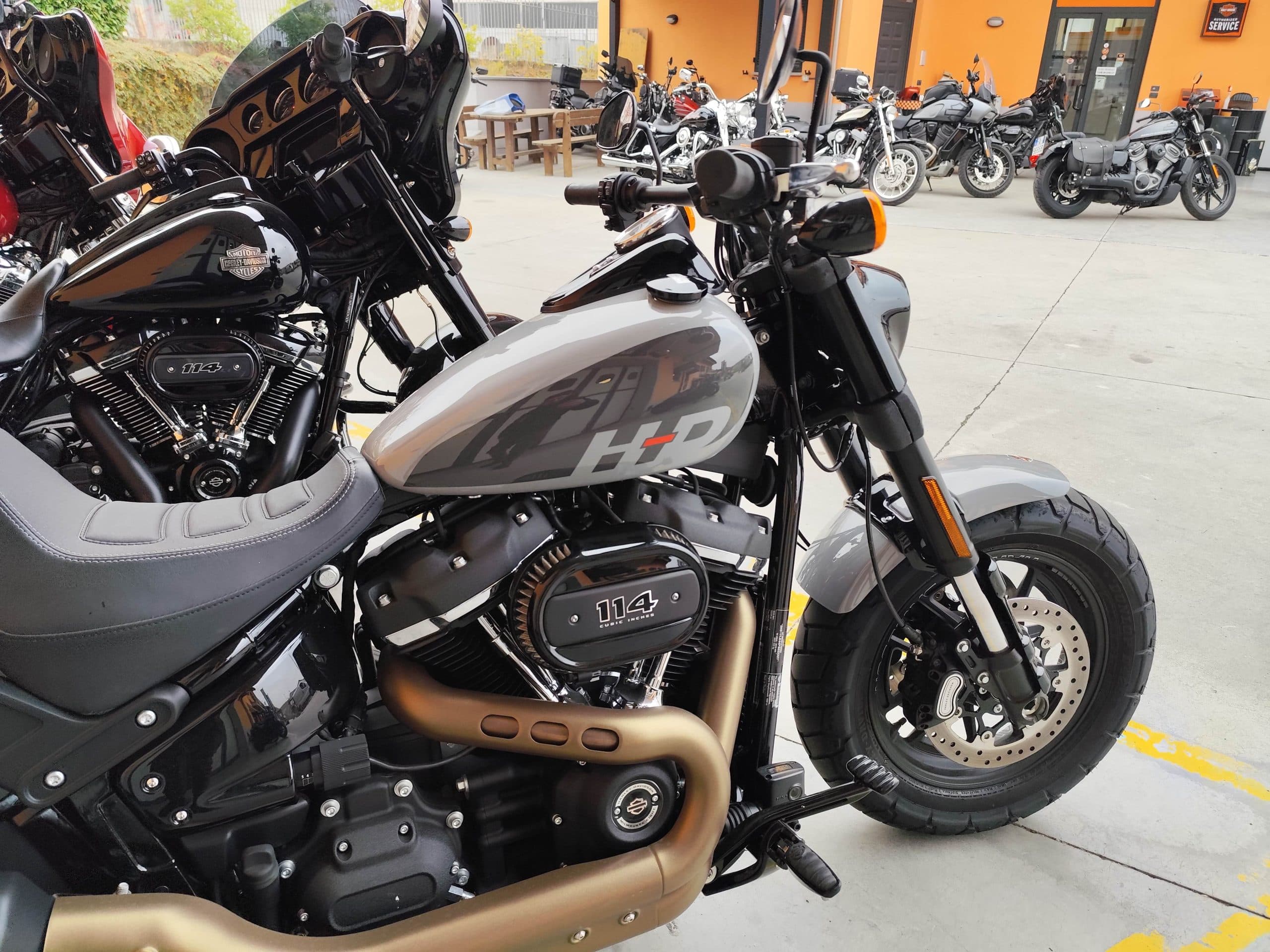 Harley-Davidson Fat Bob 114 grigia, con motore Milwaukee-Eight 114 e scarichi bronzo, esposta all'esterno della concessionaria.