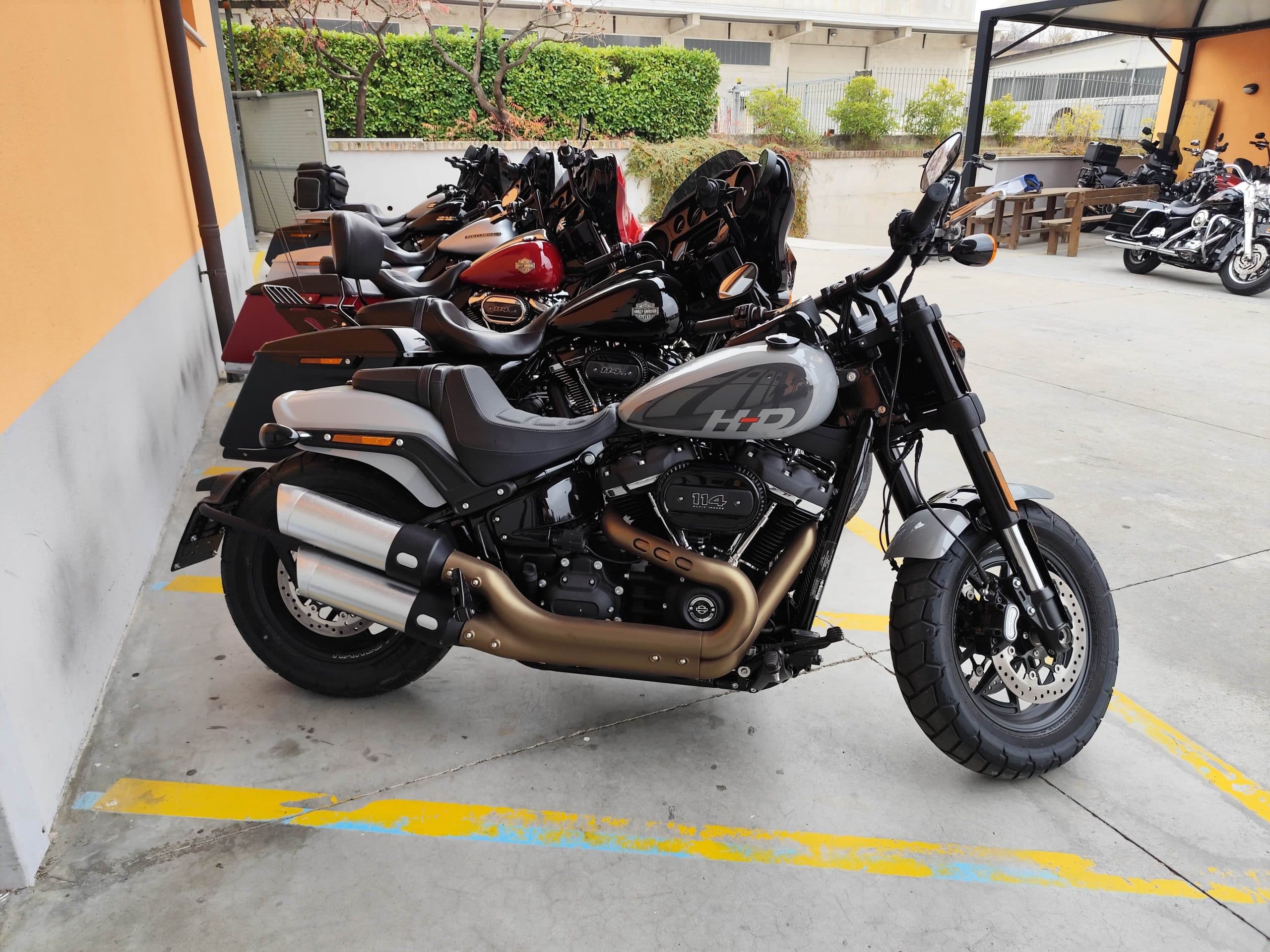 Parcheggio esterno con diverse moto Harley-Davidson, inclusa una Fat Bob 114 grigia in primo piano, pronte per test ride presso la concessionaria.