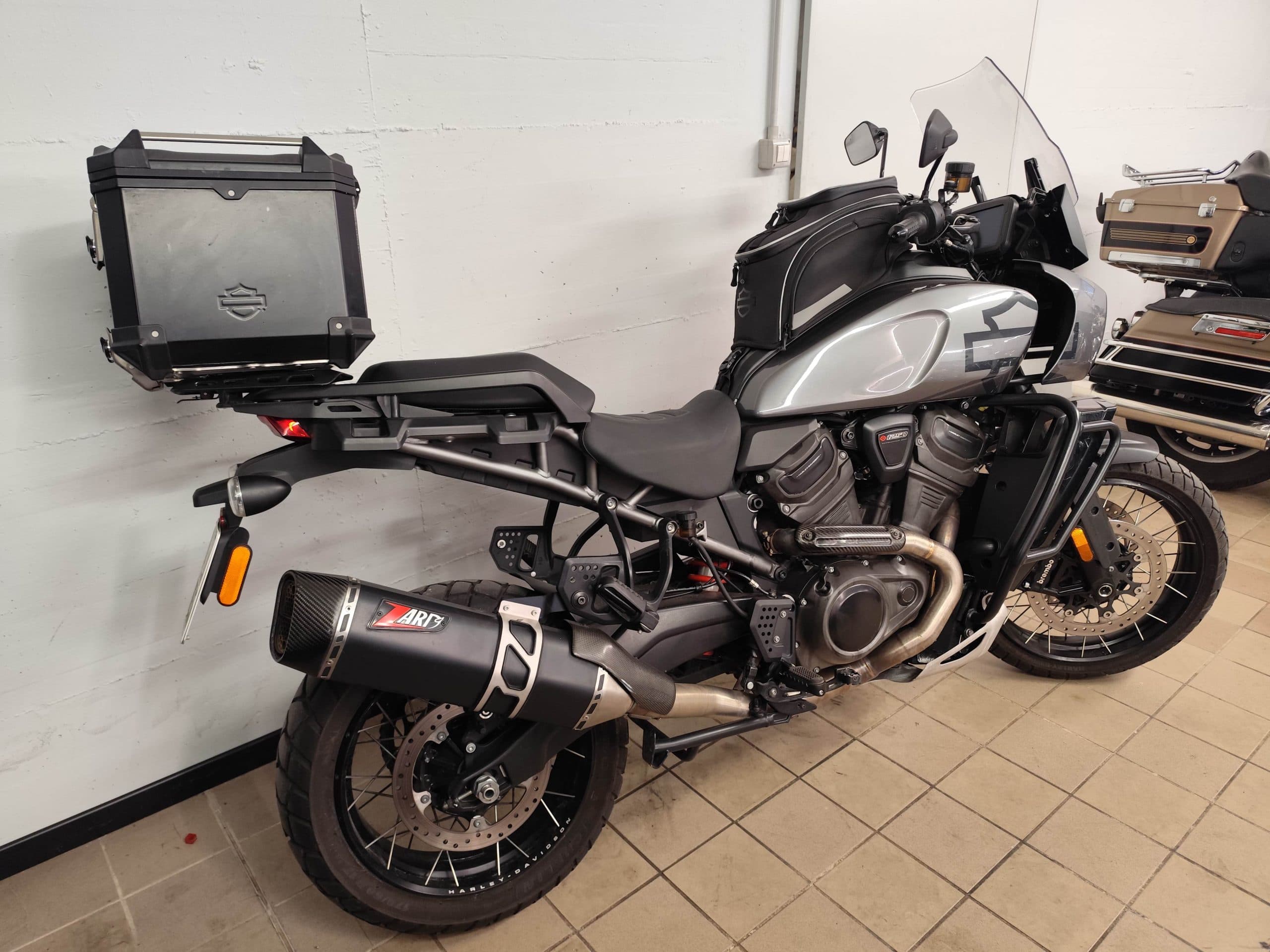 Harley-Davidson Pan America 1250 Special grigia con bauletto posteriore nero, borsa da serbatoio, scarico Zard e cerchi a raggi, parcheggiata in un garage.