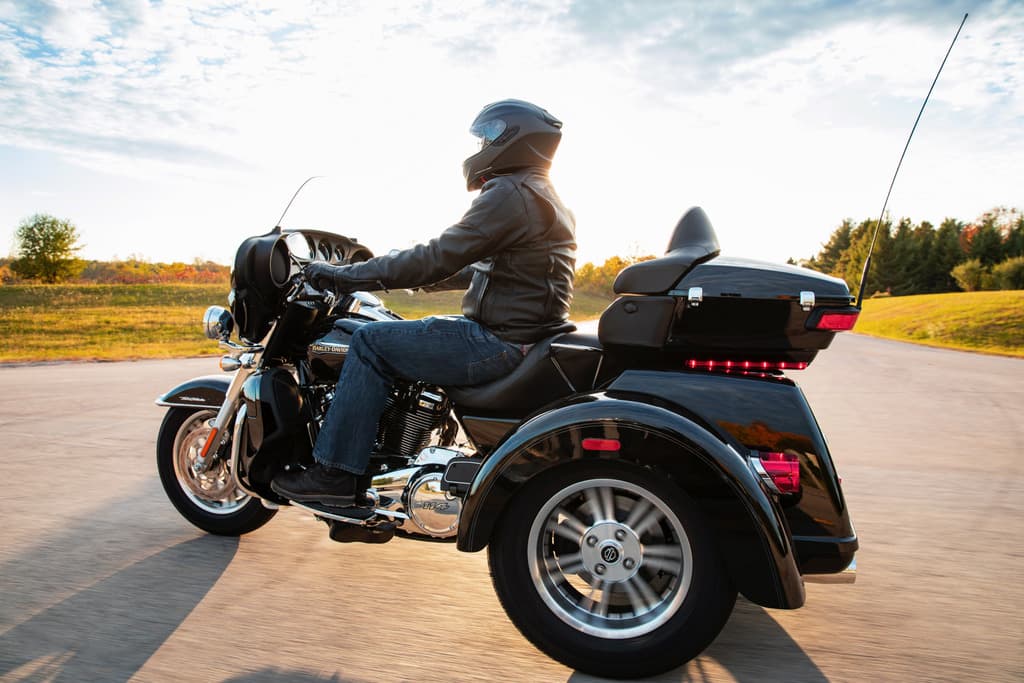 Harley-Davidson Tri Glide Ultra nera in movimento su strada, guidata da un motociclista con casco e abbigliamento tecnico. Ideale per test ride.