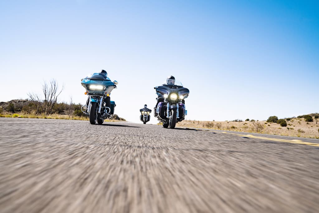Tre motociclette Harley-Davidson in movimento su strada aperta, con effetto panning che accentua la dinamicità della guida e l'esperienza di viaggio.