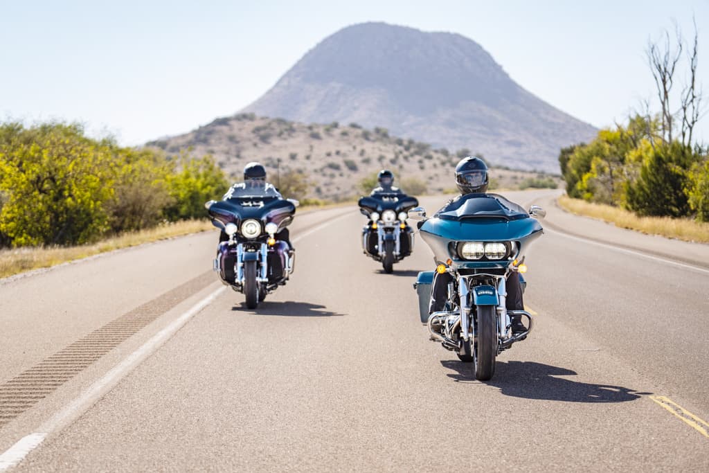 Tre moto Harley-Davidson touring in formazione su strada. Piloti con abbigliamento tecnico e caschi. Sfondo montano, ideale per un test ride.