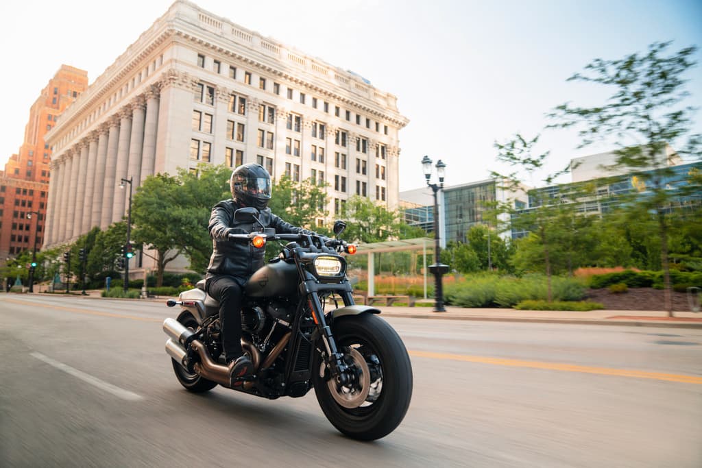 Motociclista con casco integrale e abbigliamento tecnico in pelle nera in sella a una Harley-Davidson su strada urbana. Perfetta per un test ride.