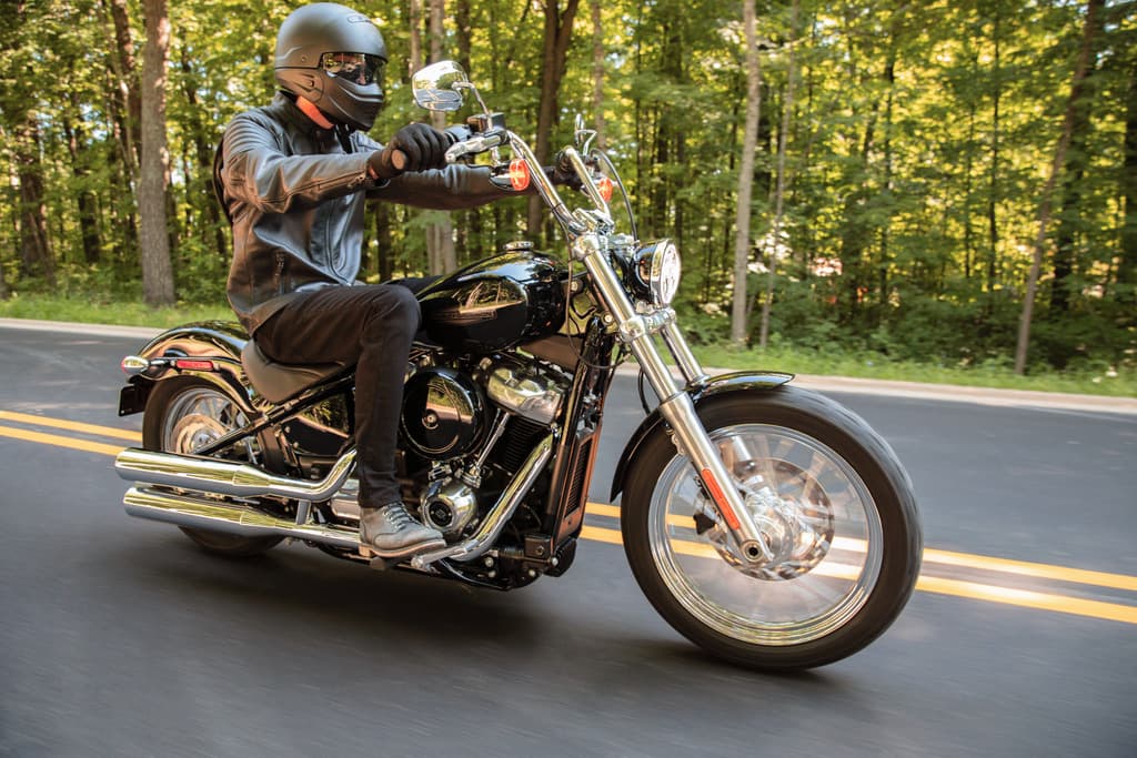 Motociclista con abbigliamento tecnico su moto Harley-Davidson nera, modello cruiser, in movimento su strada panoramica. Perfetta per test ride.