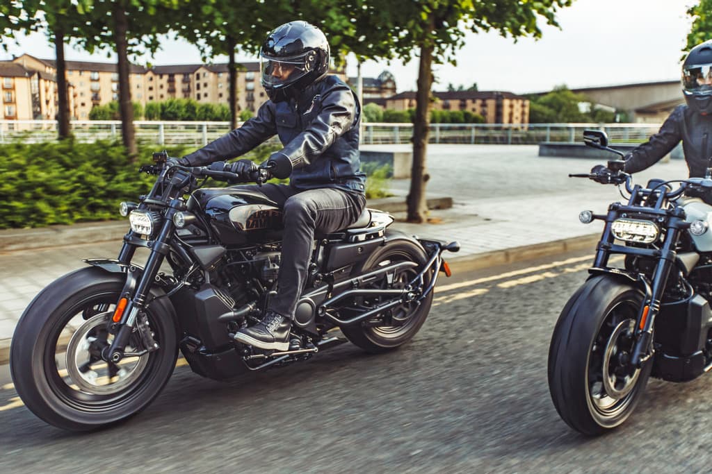 Motociclista con abbigliamento tecnico e casco su una moderna Harley-Davidson nera in movimento. Un secondo motociclista segue. Scena dinamica di test ride.