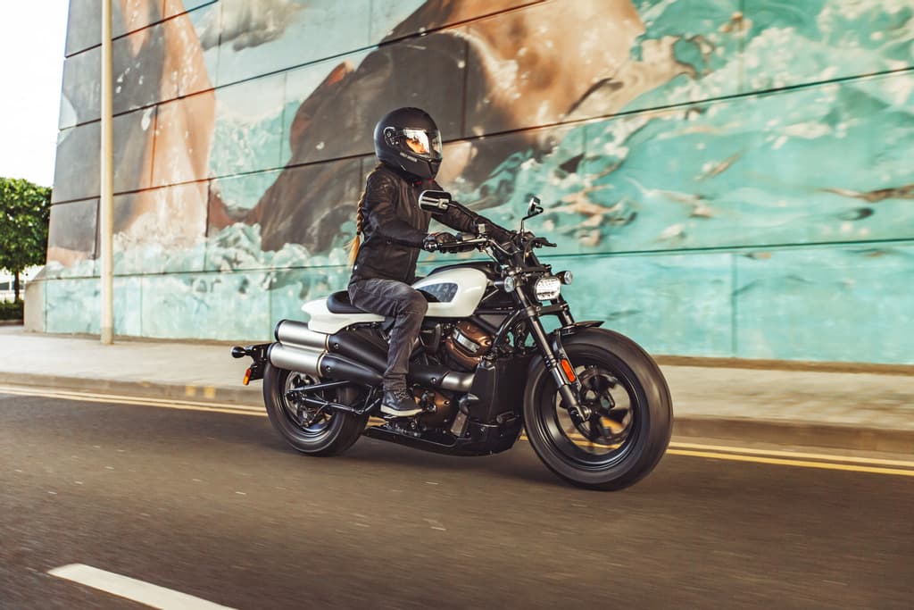 Harley-Davidson Sportster S bianca con motociclista in abbigliamento tecnico e casco integrale durante un test ride su strada urbana.