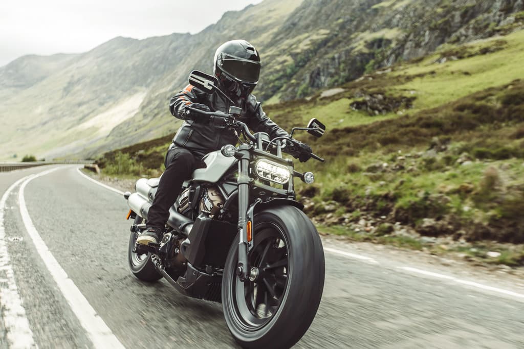 Pilota con abbigliamento tecnico Harley-Davidson in sella a una moto Sportster S su strada di montagna, ideale per un test ride.