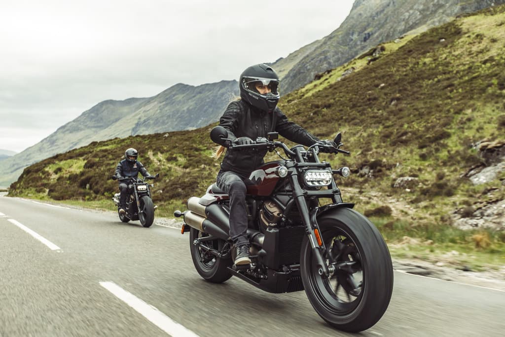 Donna in casco e abbigliamento tecnico guida moto Harley-Davidson Sportster S su strada montana, seguita da altro motociclista. Perfetto per test ride.