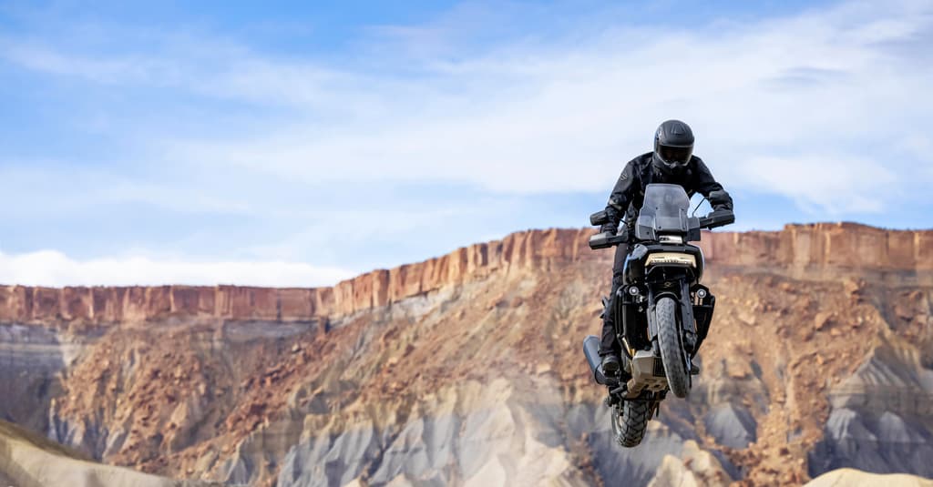 Harley-Davidson Pan America in salto off-road con pilota in abbigliamento tecnico. Sfondo di canyon desertici. Scopri la moto e i motori.