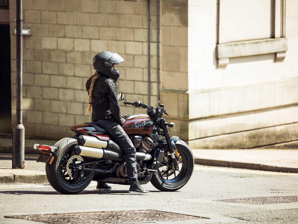 Motociclista con casco e abbigliamento tecnico su moto Harley-Davidson, in sosta su strada urbana.