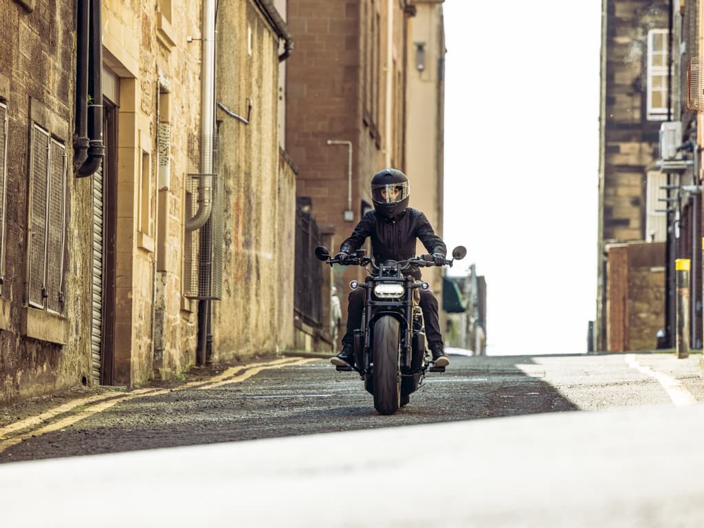 Rider con casco integrale e abbigliamento tecnico su moto Harley-Davidson, in movimento su una strada urbana stretta. Ideale per test ride.