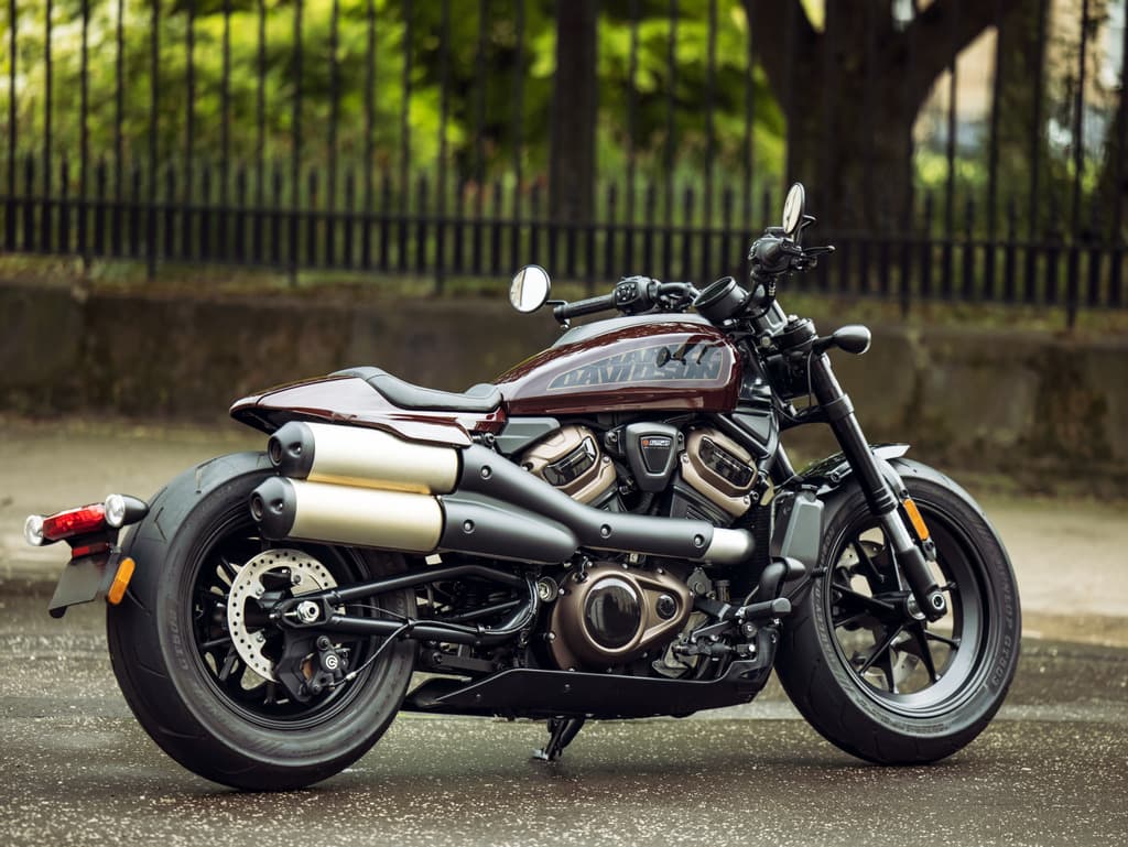 Harley-Davidson Sportster S bordeaux parcheggiata su strada bagnata. Dettagli motore Revolution Max 1250T, scarichi alti e design moderno.