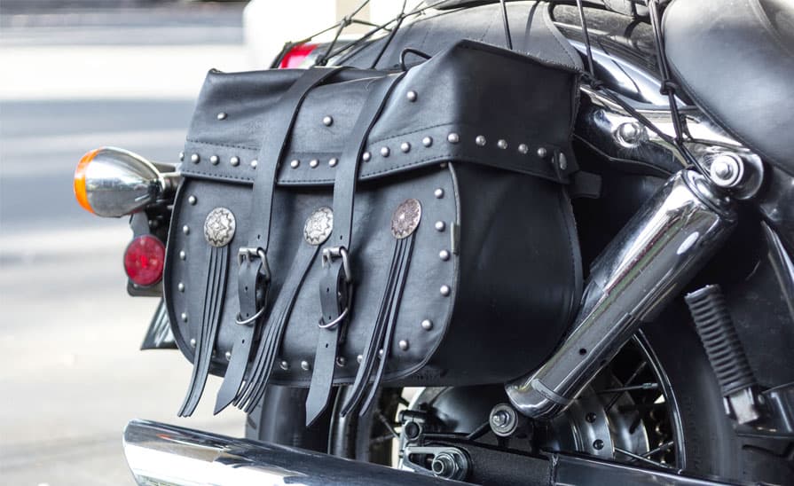 Borsa laterale in pelle nera borchiata con conchos, montata sul parafango posteriore di una moto cruiser Harley-Davidson.