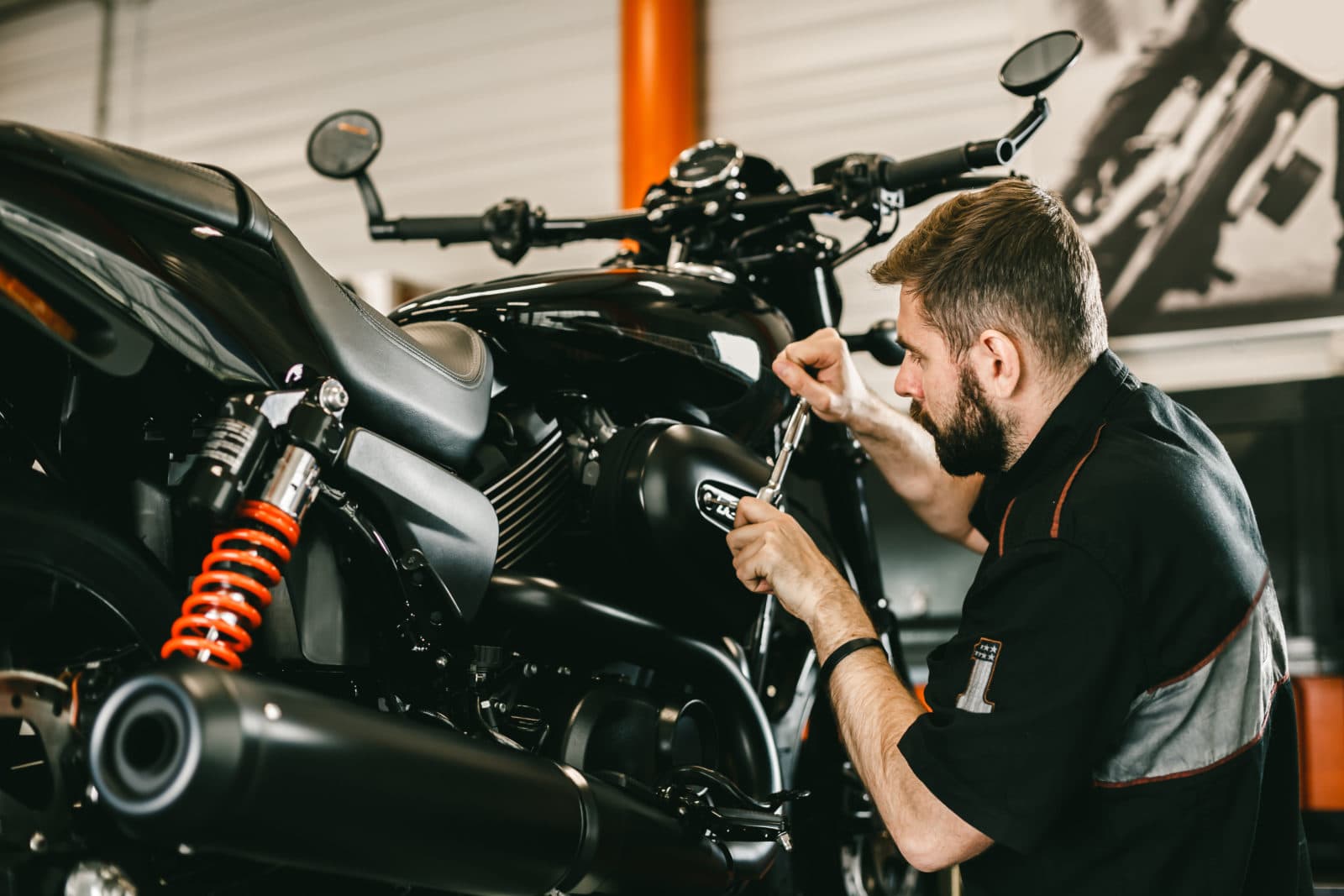Meccanico specializzato esegue manutenzione su una moto Harley-Davidson nera, utilizzando una chiave a bussola per un intervento sul motore.