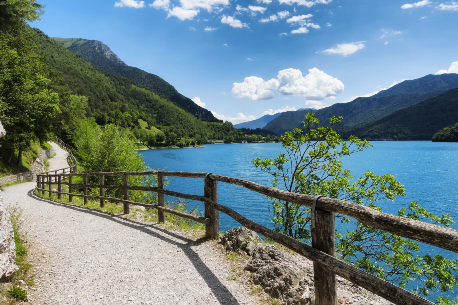 Paesaggio montano con lago alpino azzurro e sentiero ghiaioso. Scenario ideale per avventure e test ride in moto Harley-Davidson.
