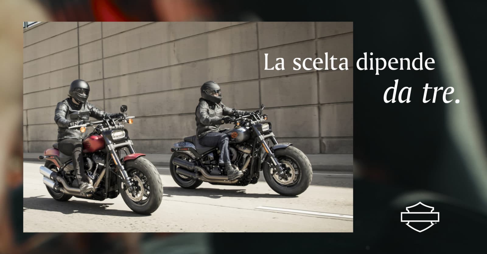 Due motociclisti su diverse Harley-Davidson, una rossa e una scura, con abbigliamento tecnico. Il testo suggerisce una scelta tra modelli.
