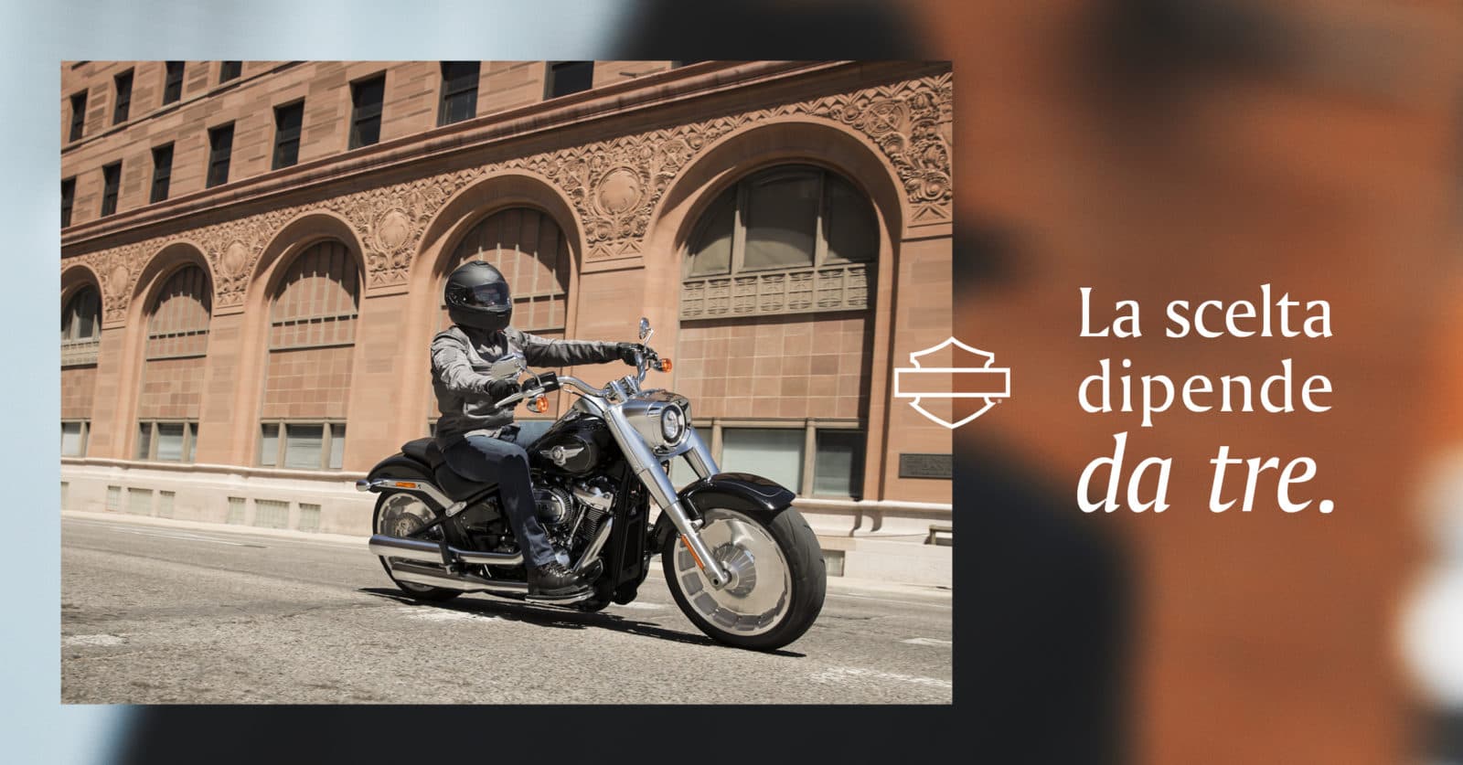 Motociclista con casco su moto Harley-Davidson nera in contesto urbano, affiancato dal logo Harley-Davidson e testo "La scelta dipende da tre.".