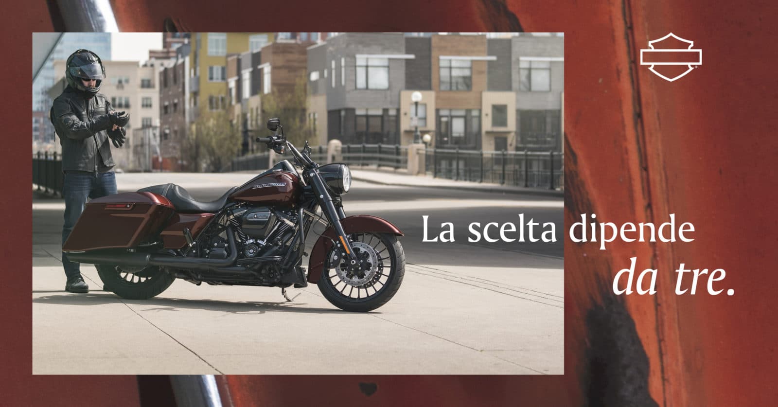 Motociclista con casco e abbigliamento tecnico Harley-Davidson, si prepara accanto a una moto touring rossa. Logo Harley-Davidson.