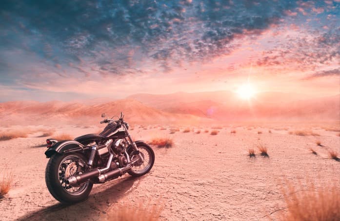 Harley-Davidson in un vasto paesaggio desertico al tramonto, con cielo drammatico e sole splendente. Incarna lo spirito di avventura e i motori potenti.