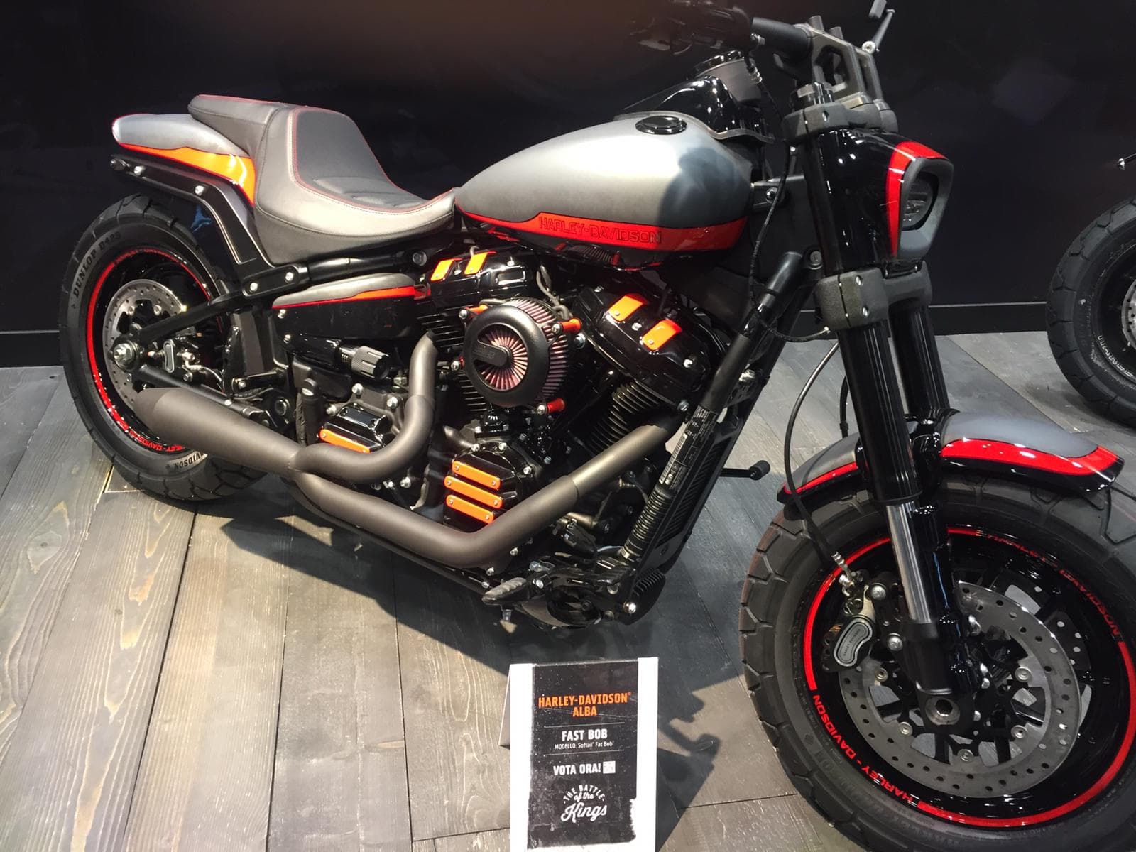 Harley-Davidson Fast Bob customizzata, modello Softail Fat Bob, con livrea grigio opaco, dettagli rossi e arancioni, esposta da Harley-Davidson Alba.