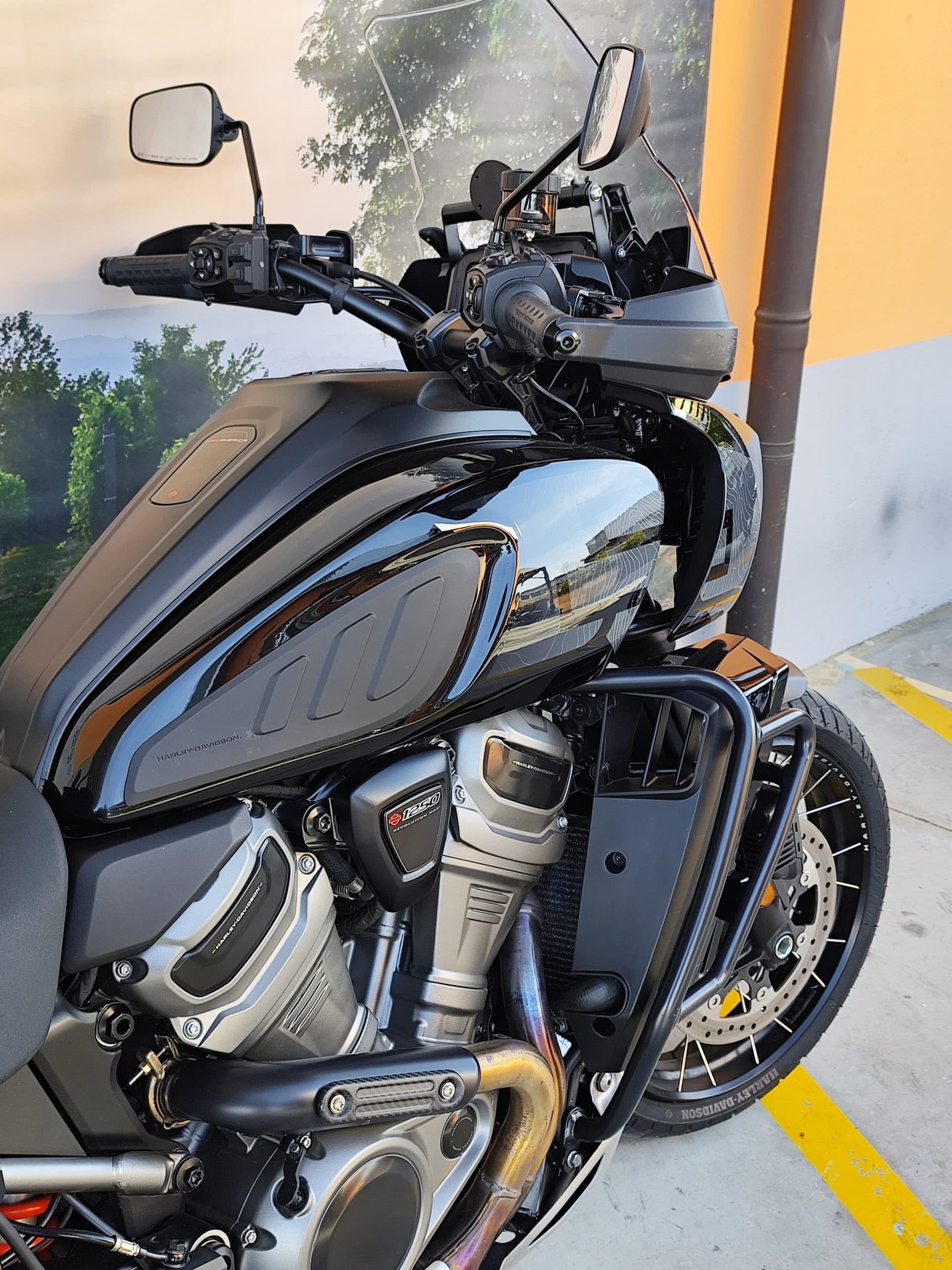 Dettaglio ravvicinato di una moto Harley-Davidson Pan America nera, evidenziando il motore Revolution Max 1250, il serbatoio e la ruota anteriore a raggi. Ideale per un test ride.