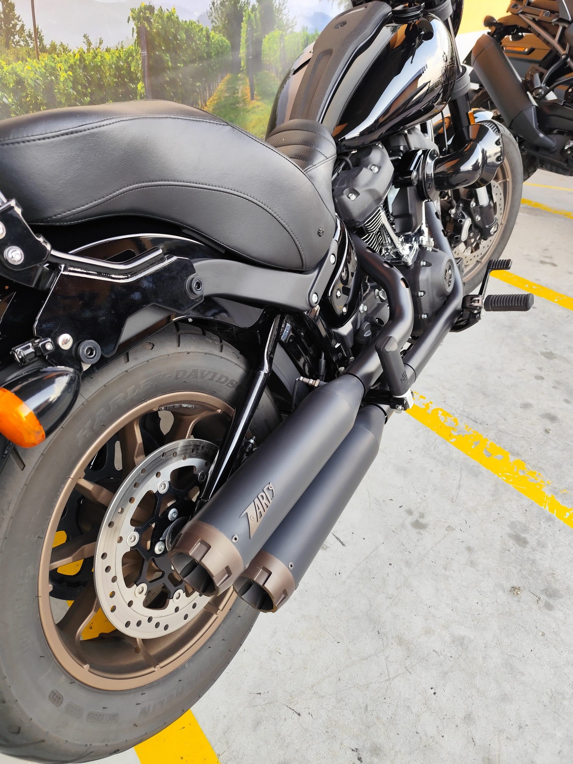 Harley-Davidson nera, vista laterale posteriore. Scarichi ZARD neri con terminali bronzo, sella in pelle, cerchio posteriore bronzo, freno a disco.