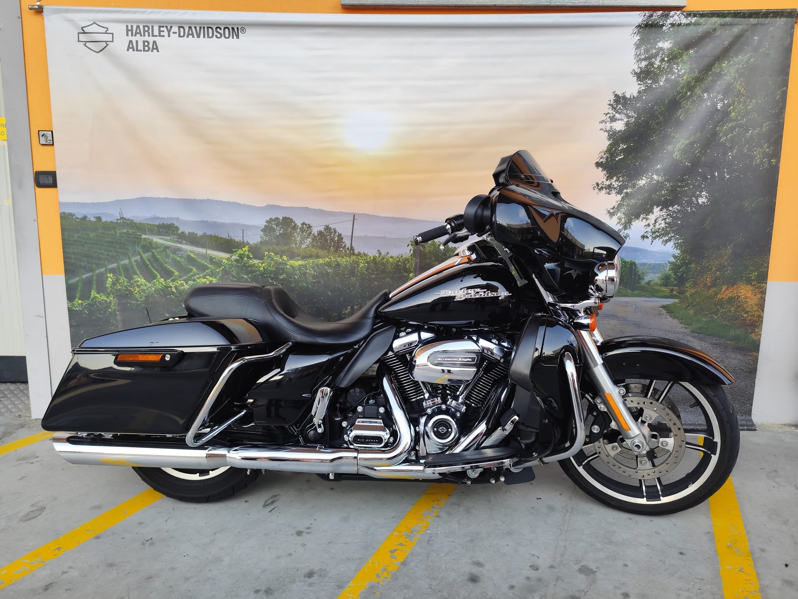 Motocicletta Harley-Davidson touring nera con motore Screamin' Eagle, in esposizione davanti al banner della concessionaria Harley-Davidson Alba.